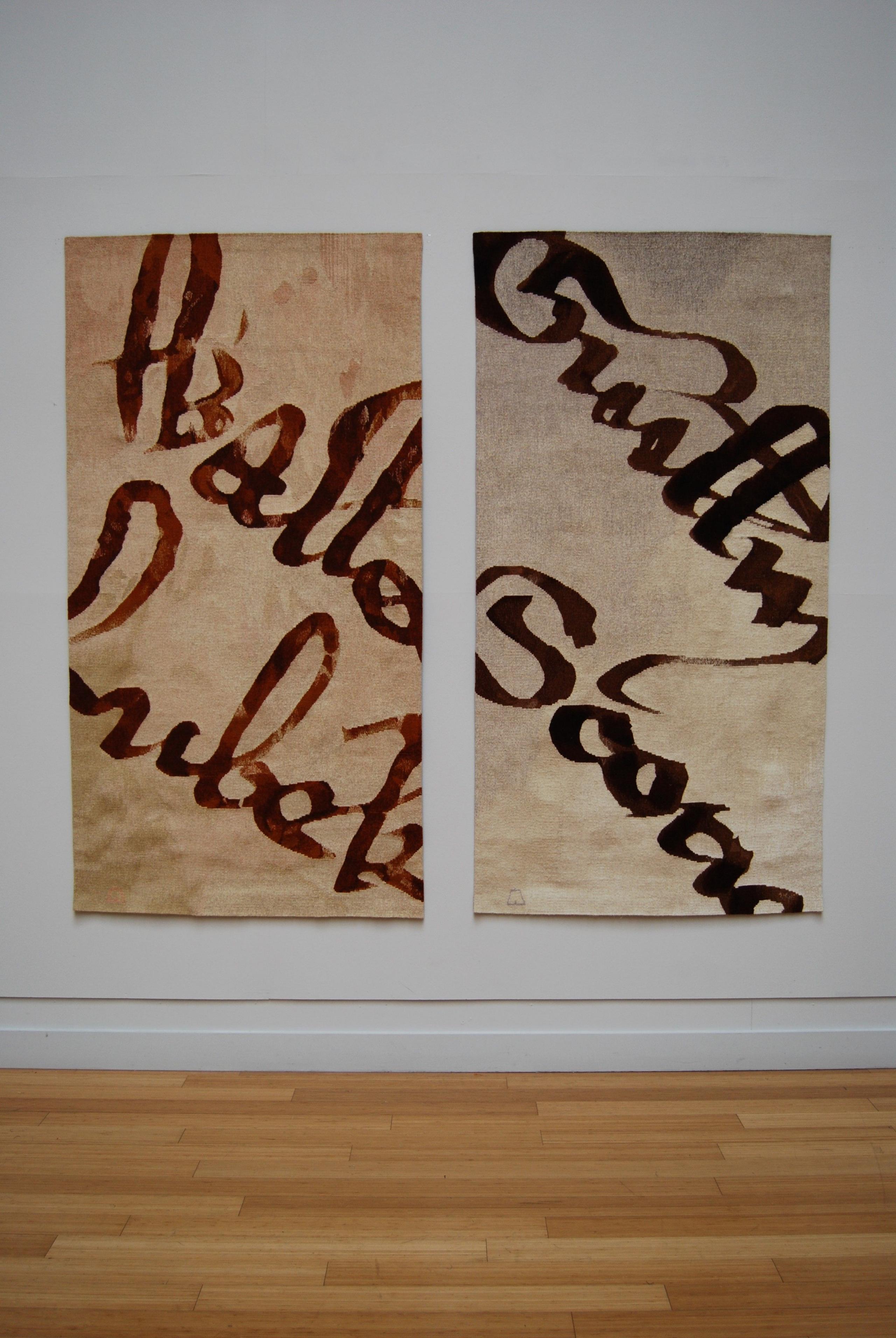 Two tapestries hanging on the wall with script letters weaved into them. 