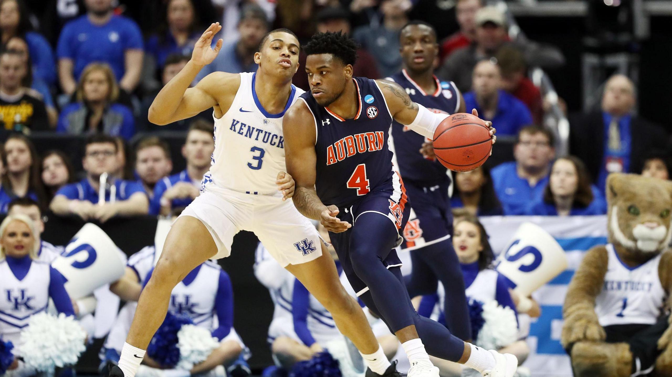 Malik Dunbar of the Auburn Tigers, in blue kit, dribbles against Keldon Johnson of the Kentucky Wildcats, in white kit, as a crowd watch on. 