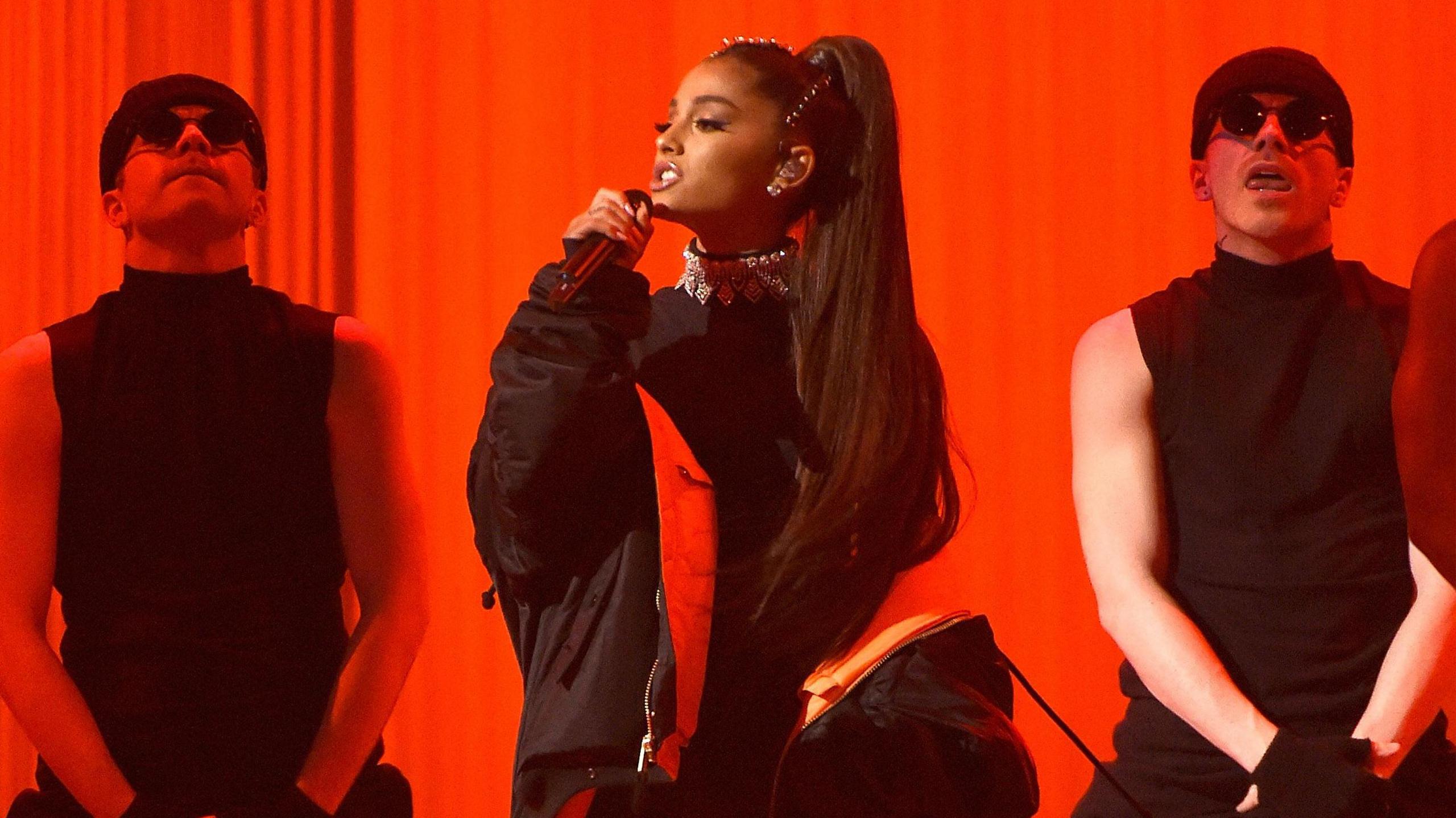 Ariana Grande singing on stage with two male dancers standing behind her 