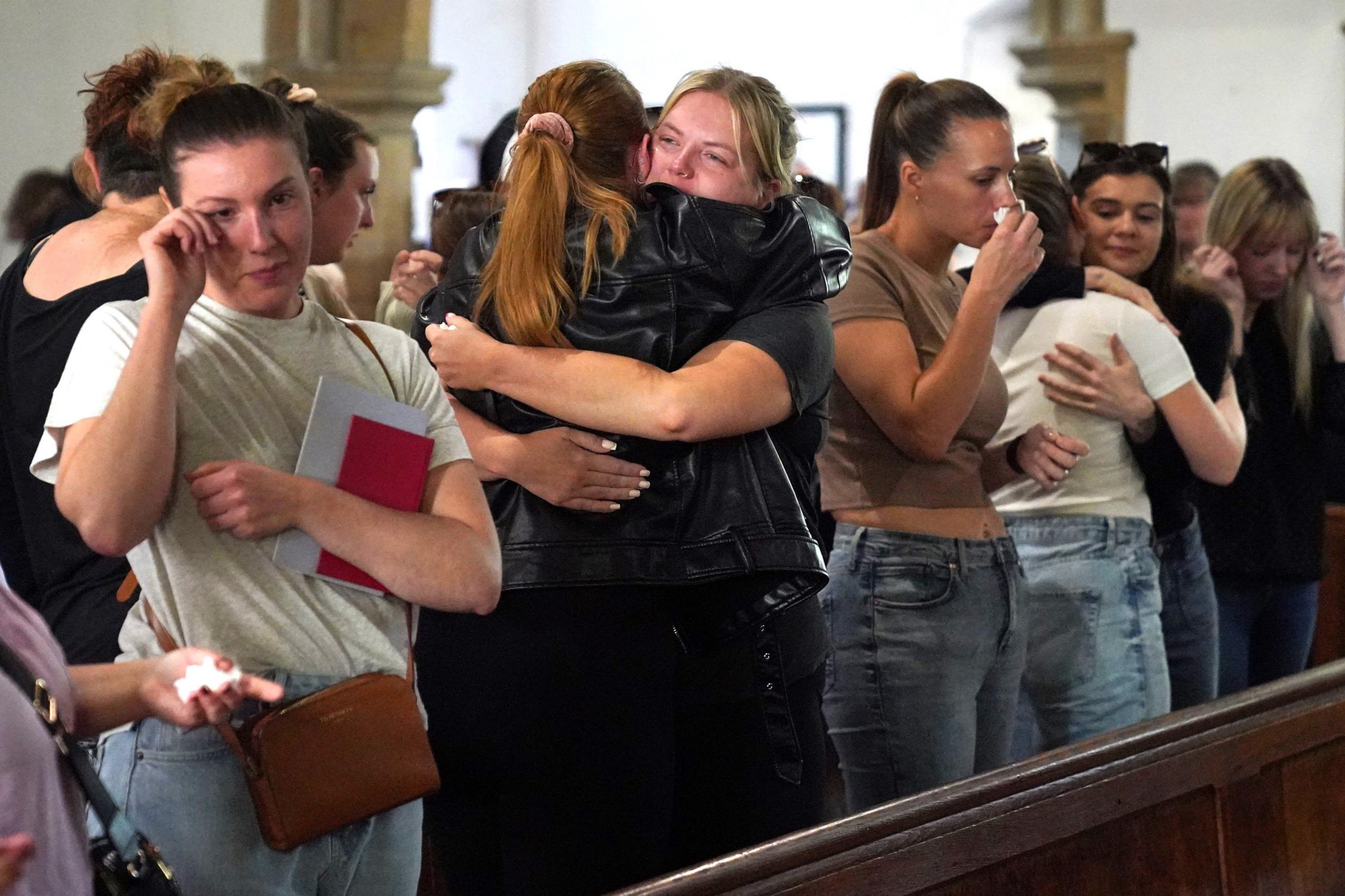 Young women are standing in the pews at the front of a church and are crying and embracing.