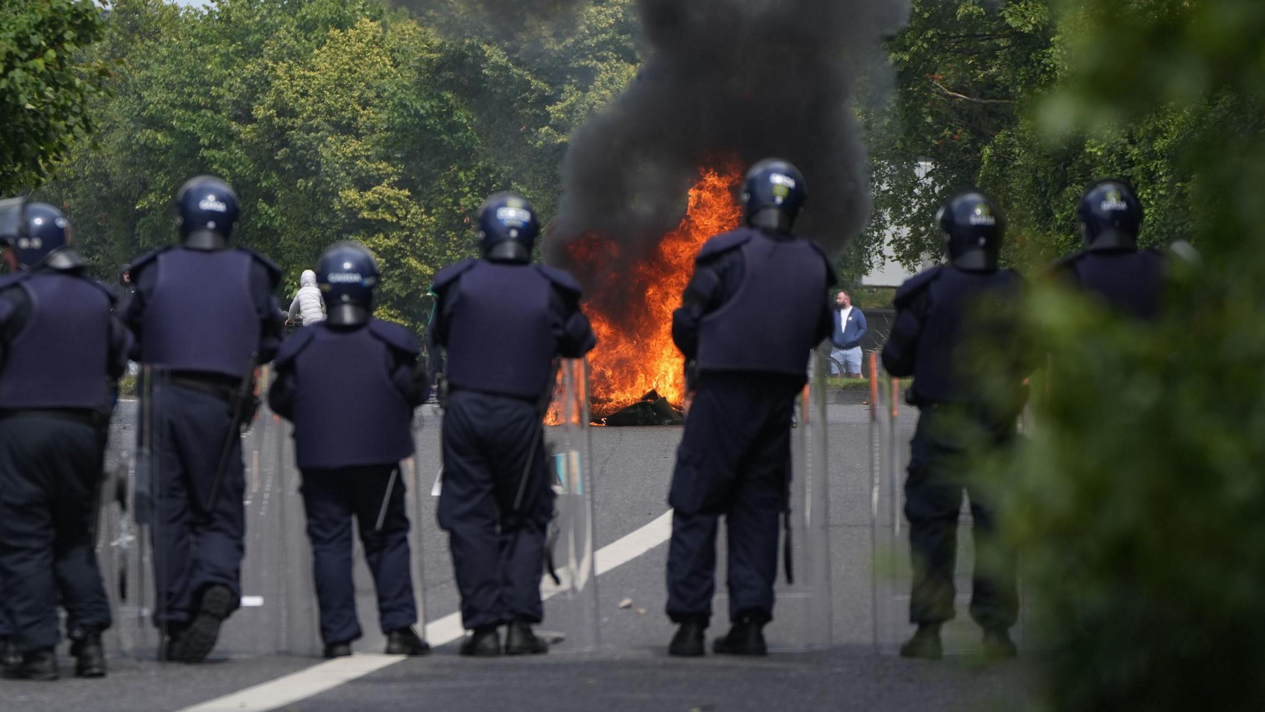 Police officers watch on as a fire is lit during the protest