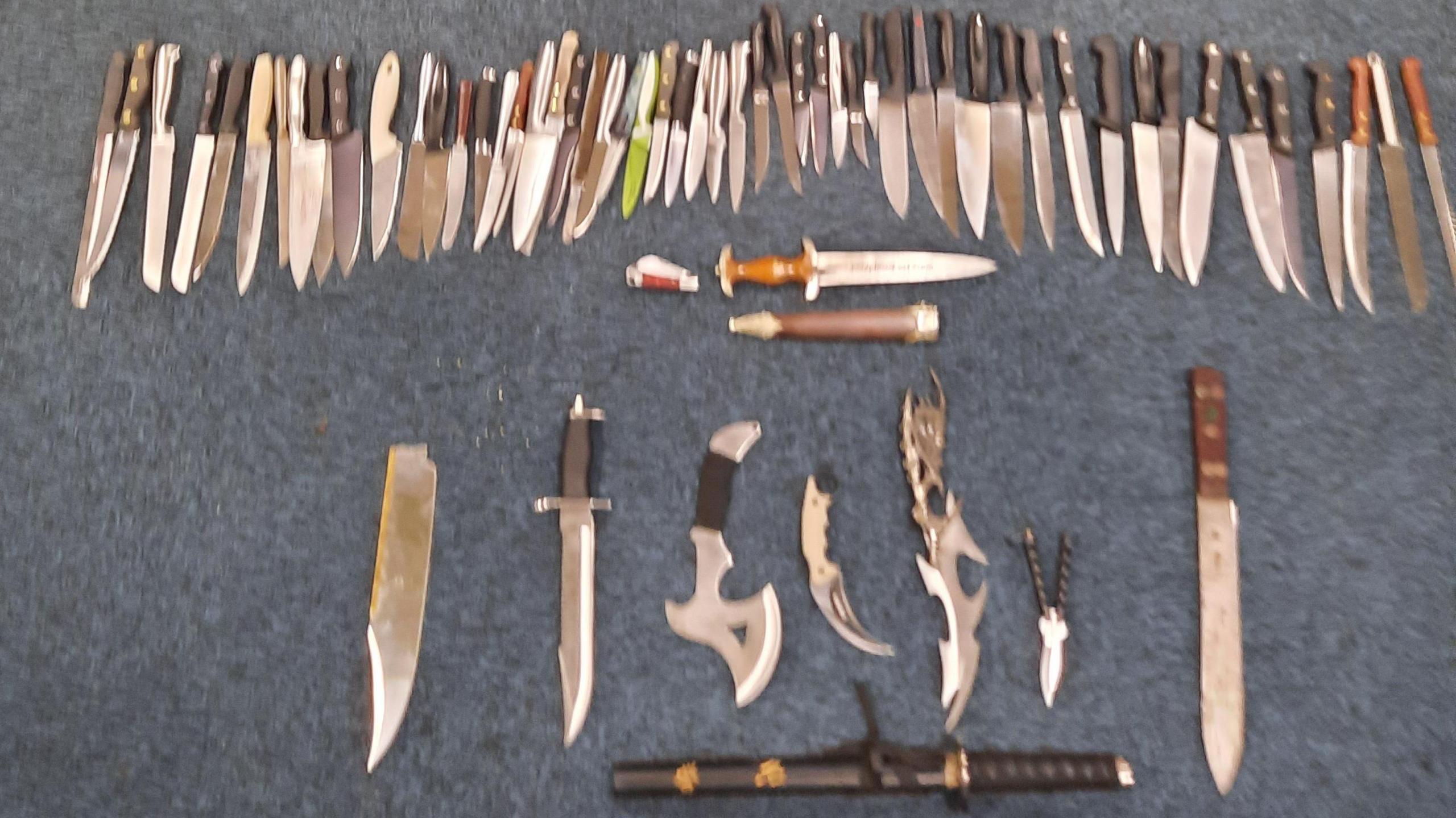 A large number of knives collected by police. The image is slightly blurred, showing a number of knives left on a blue floor. 