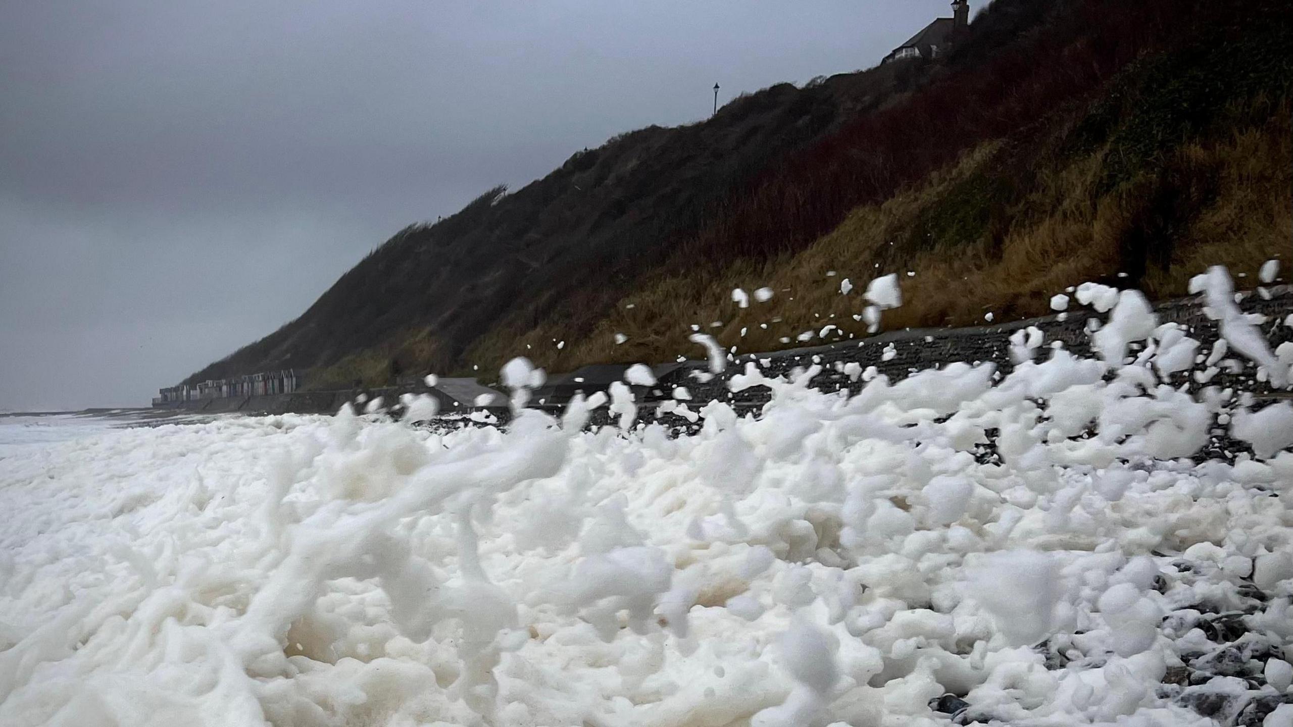 The beach at Cromer in Norfolk. Spray is coming off of the sea and a cliff can be seen in the background of the picture.