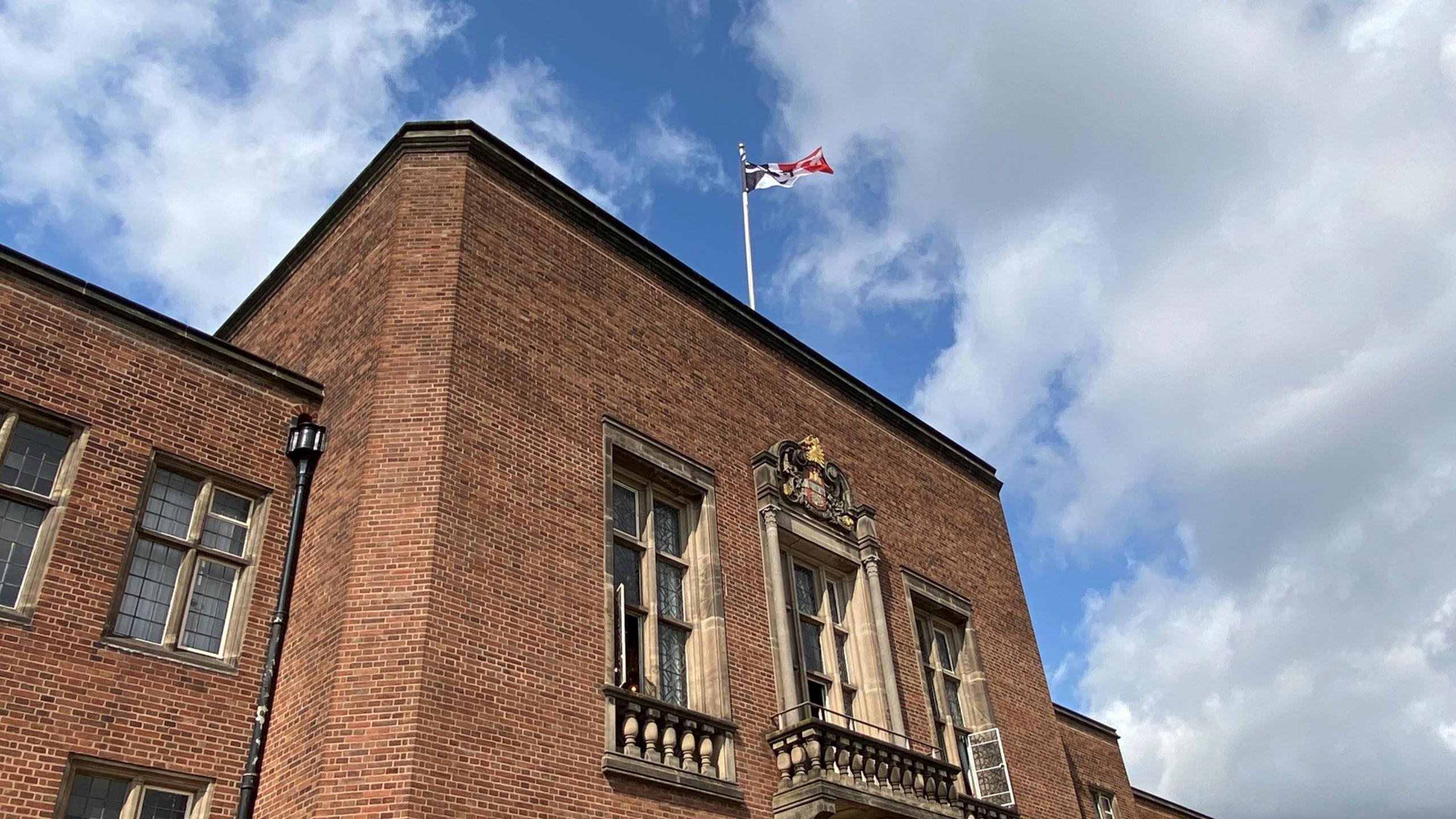 The flag of the Black Country is flying at the top of a large brick building. The flag is black, white and red with chain representing the region's manufacturing heritage.
