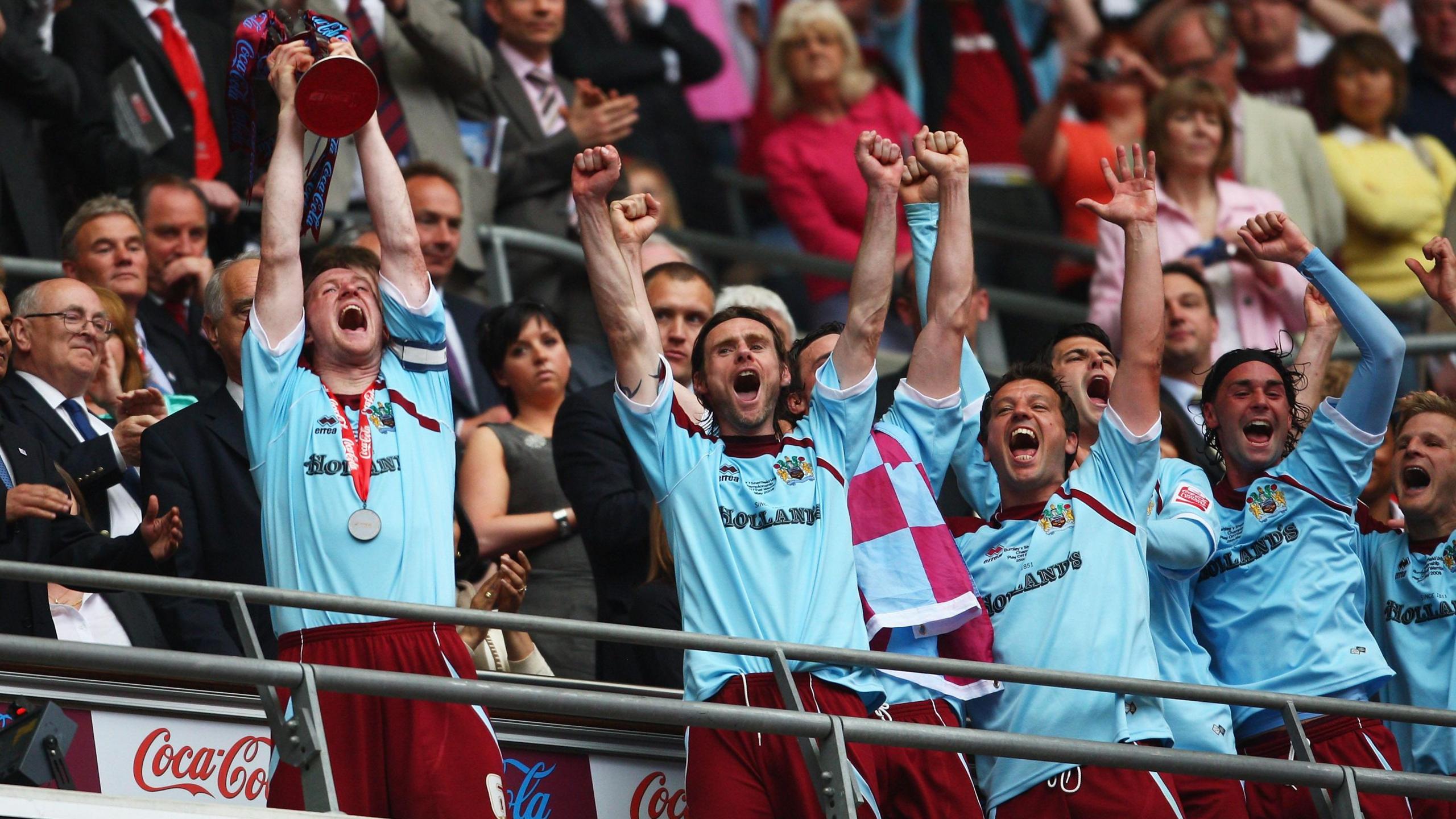 Steven Caldwell lifts the play-off final trophy above his head on the Wembley balcony. Several Burnley players have their arms raised cheering