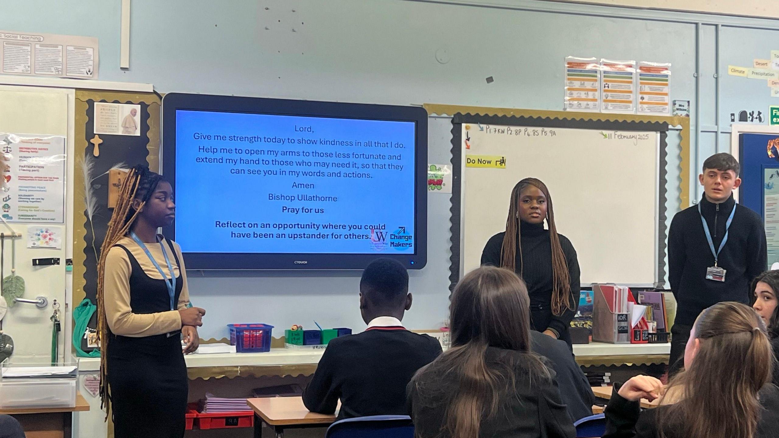 Three sixth-form students stand in front of a whiteboard large screen at the front of a classroom. Two of pupils are sat in front.