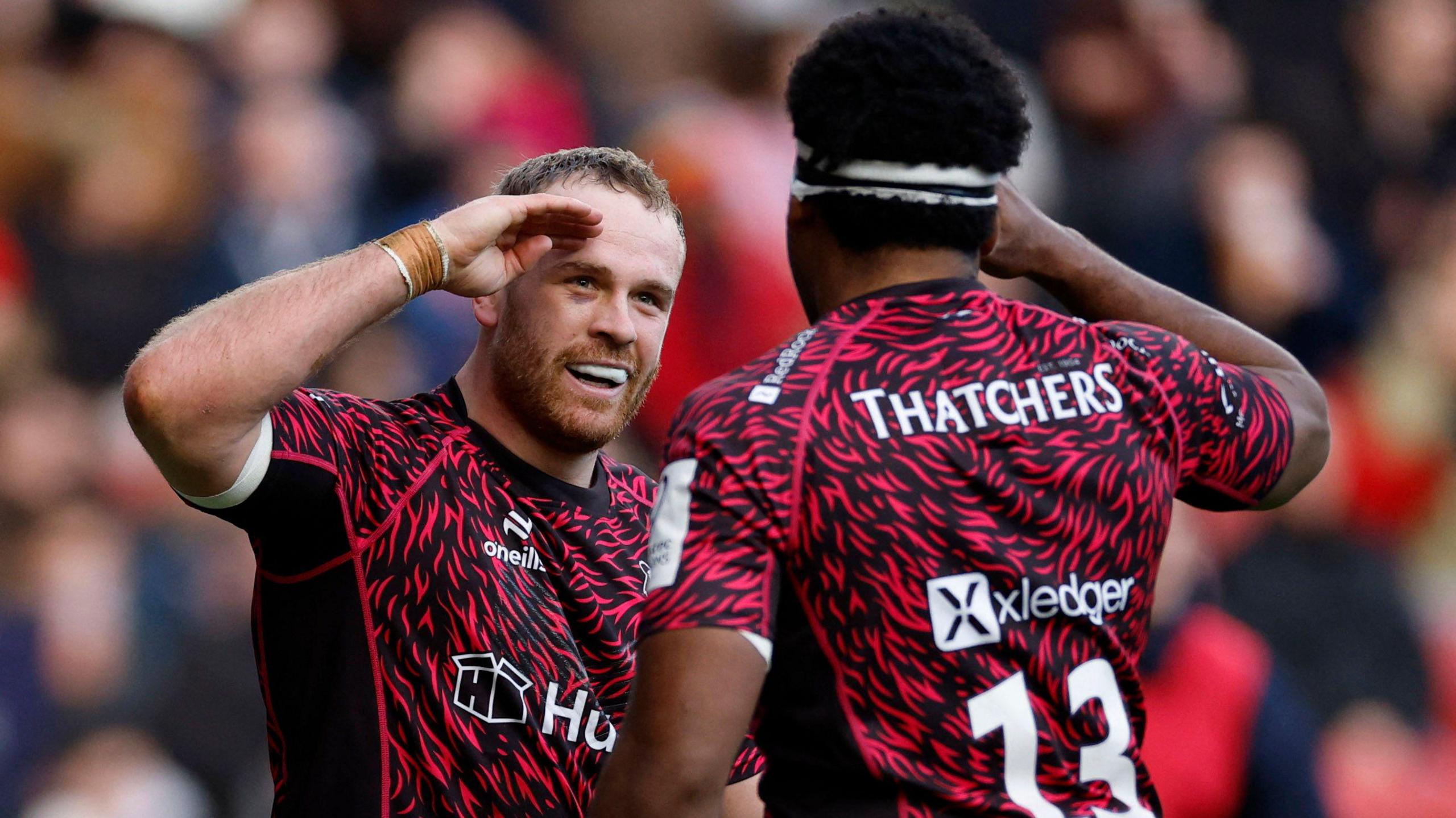 Two Bristol Bears rugby players, wearing the club's change kit of dark red with black flecks, salute each other as they celebrate a try scored against French club Benneton at Ashton Gate