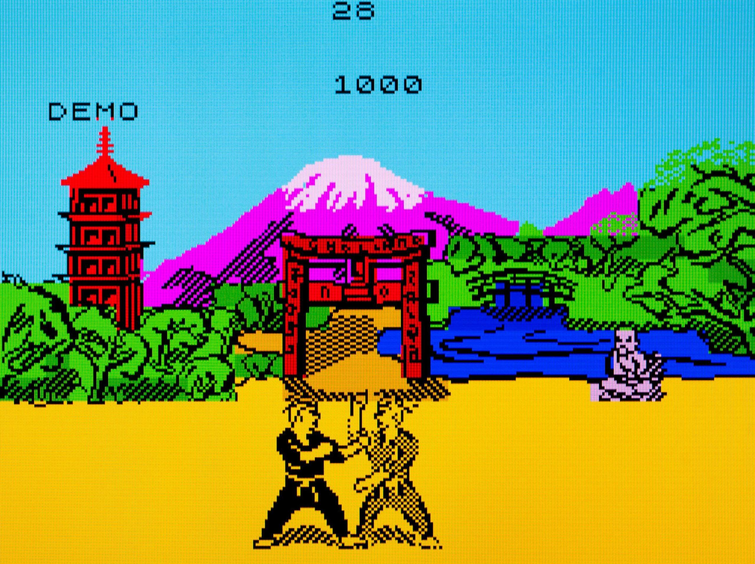 A screengrab of gameplay from The Way of the Exploding Fist. It shows two characters in martial arts clothing fighting each other. The backdrop shows a temple, shrine, mountain and another person watching the fight