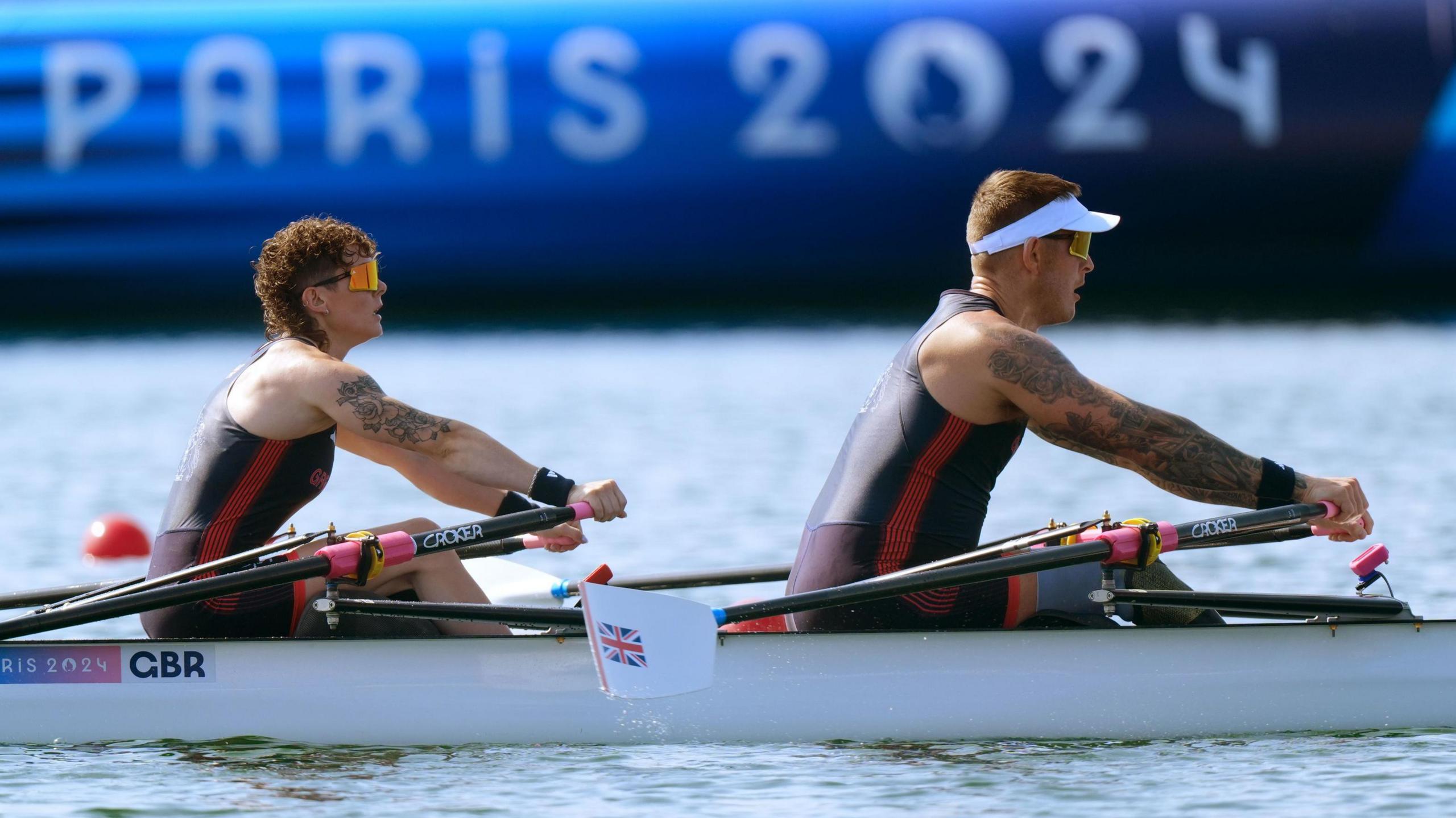 Lauren Rowles and Gregg Stevenson rowing in their boat. Lauren is wearing orange sunglasses and Gregg is wearing a white hat.