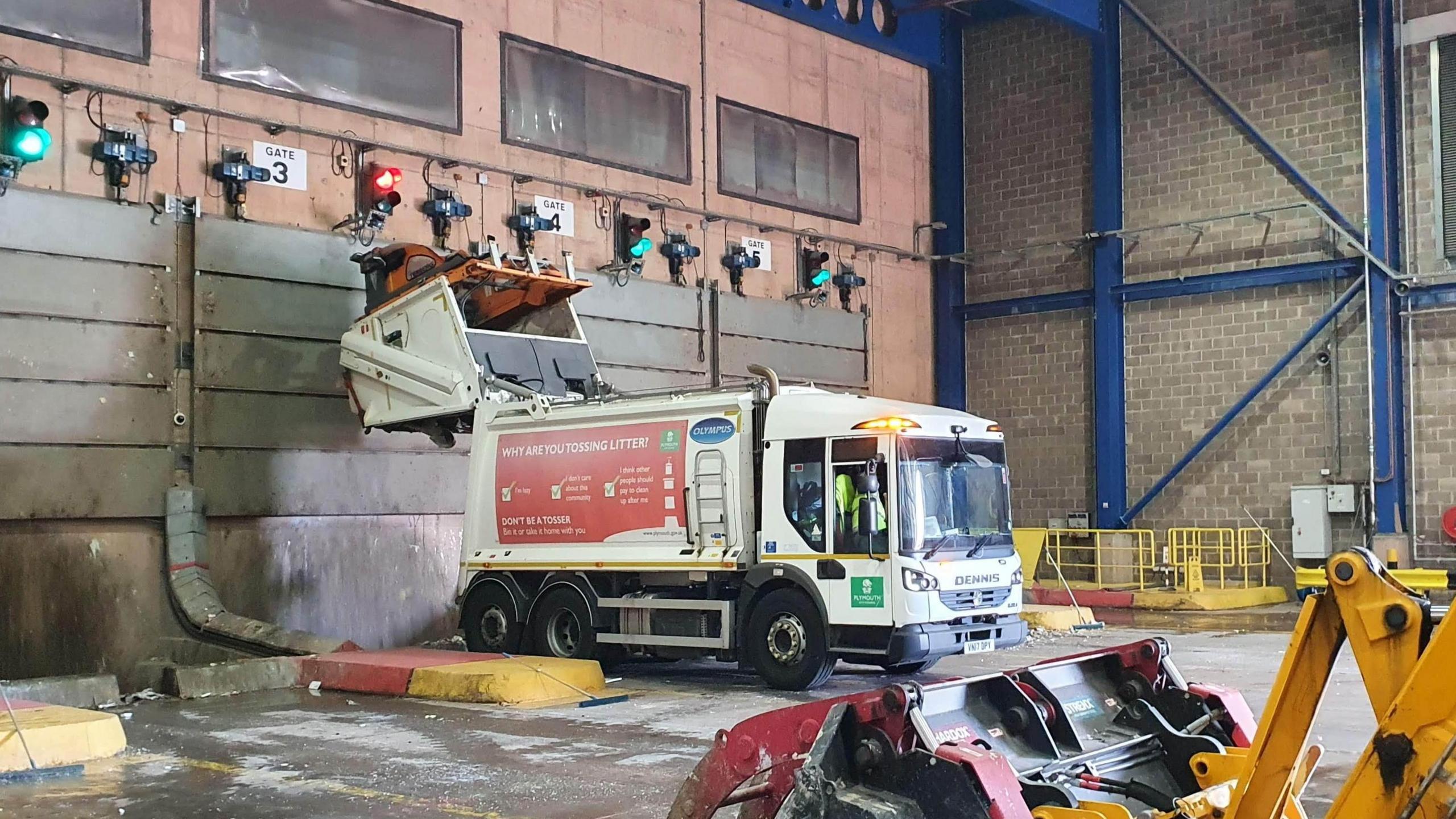  A lorry is parked up at a waste depot. The lorry is red and white.