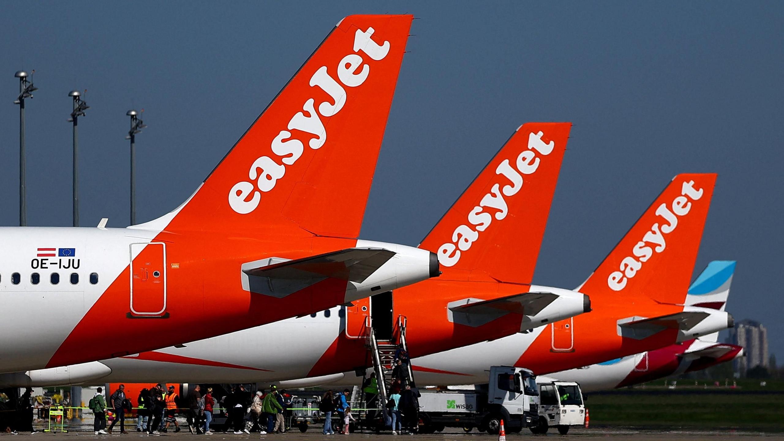 The tails of three EasyJet planes, painted red and white, parked on a runway.