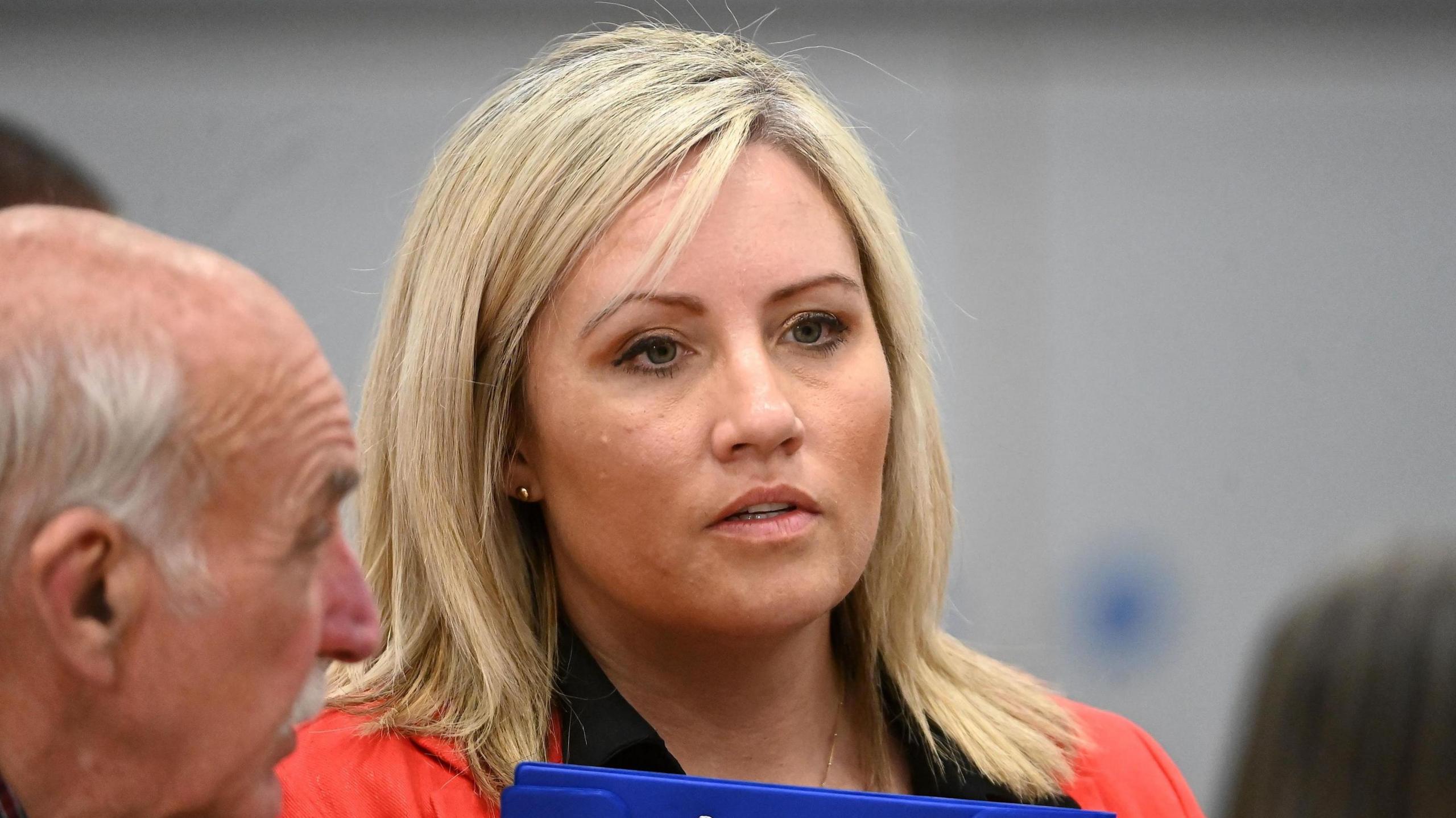 Diane Forsythe, attends the count at the South Lake Leisure Centre in Craigavon, Co Armagh, as counting begins for the 2024 General Election, she has blonde hair and is wearing a red blazer with black shirt and is holding a blue clipboard.