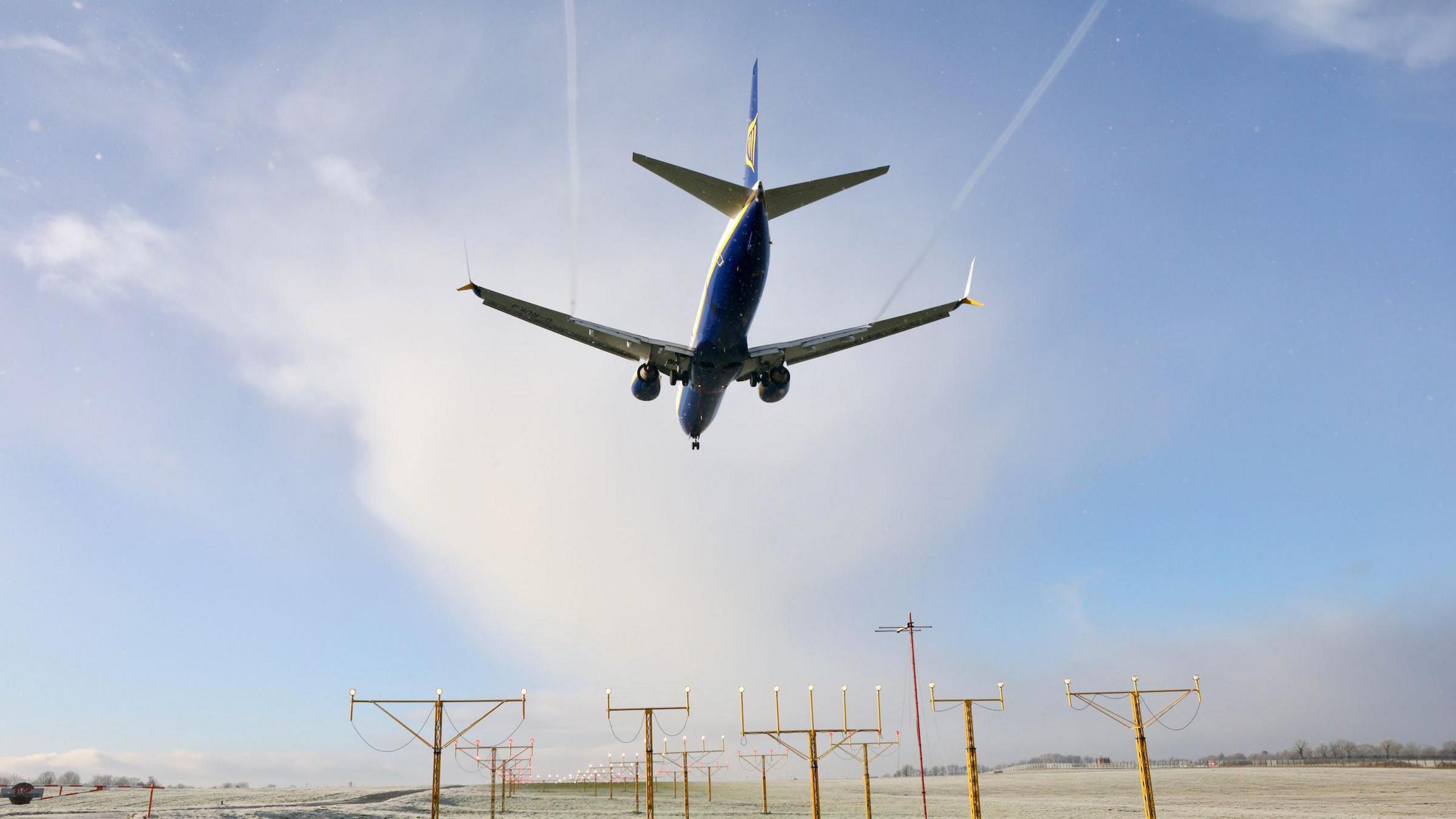 A passenger plane is seen from underneath as it flies over a number of electricity pylons near belfast airport