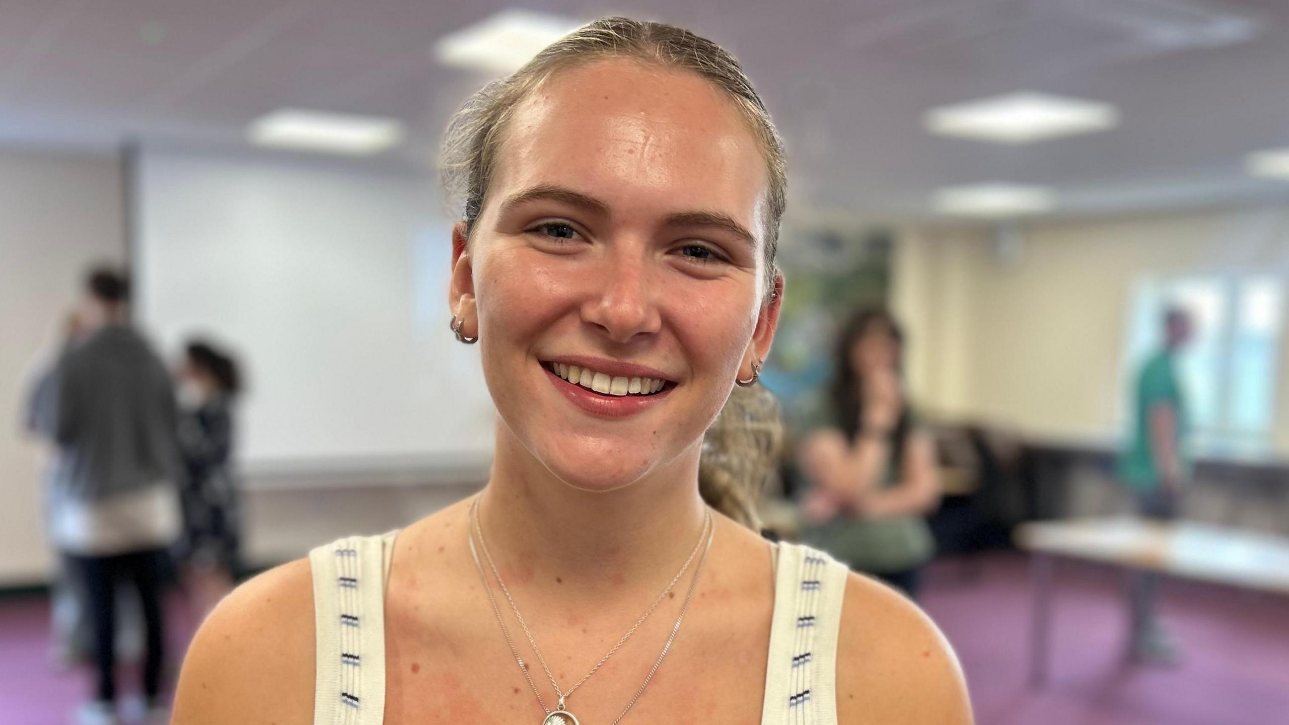 Amy Gelling smiles, she wears a blue and white striped vest with silver necklaces. Her hair is tied back in a ponytail.