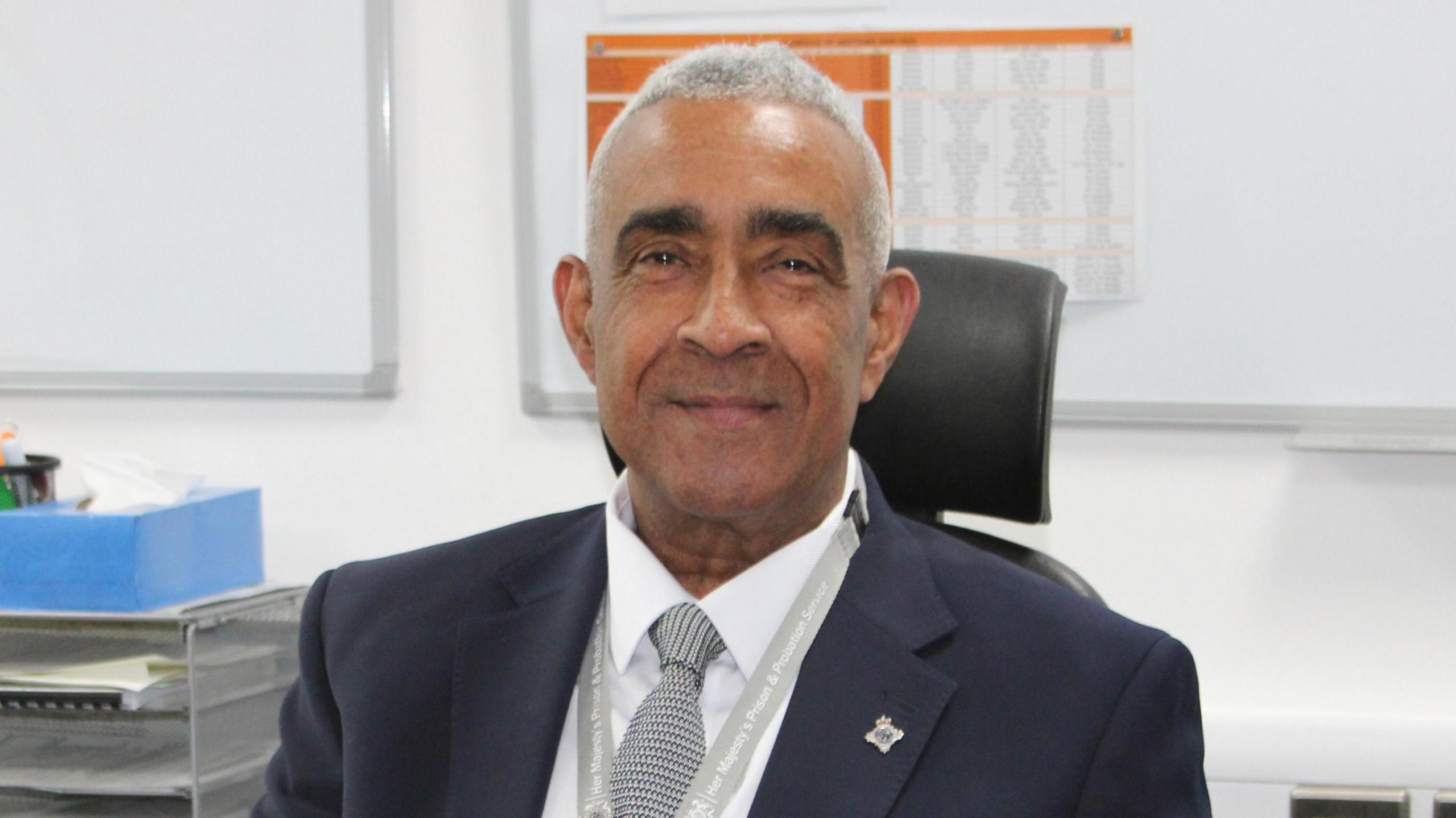 Paul Yates is wearing a dark suit and smiling at the camera while sat behind a desk.