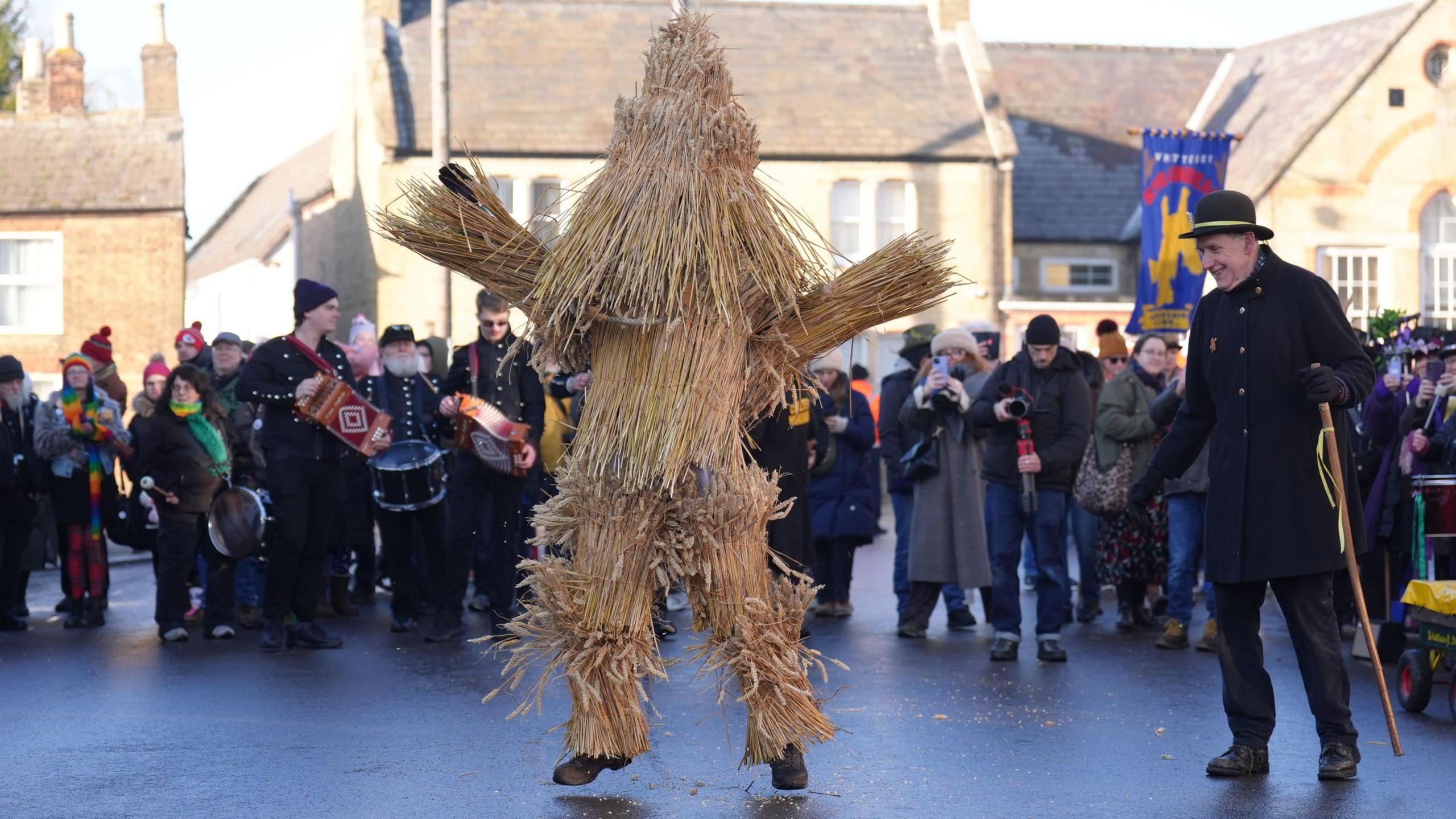 A man dressed as a straw animal in front of a crowd. 