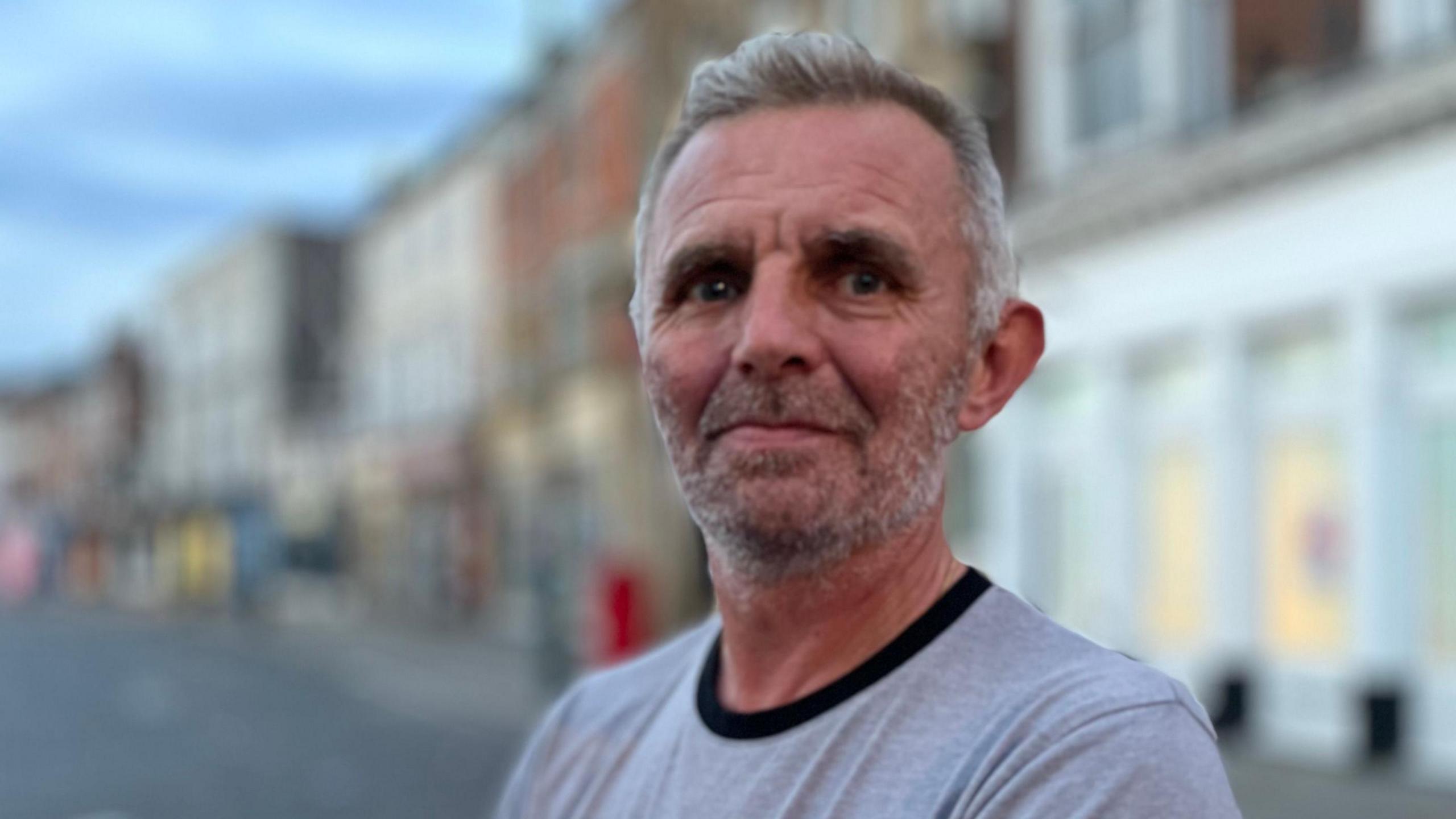 Thierry Condette, with grey stubble and hair, looks into the camera. He wears a grey t-shirt.