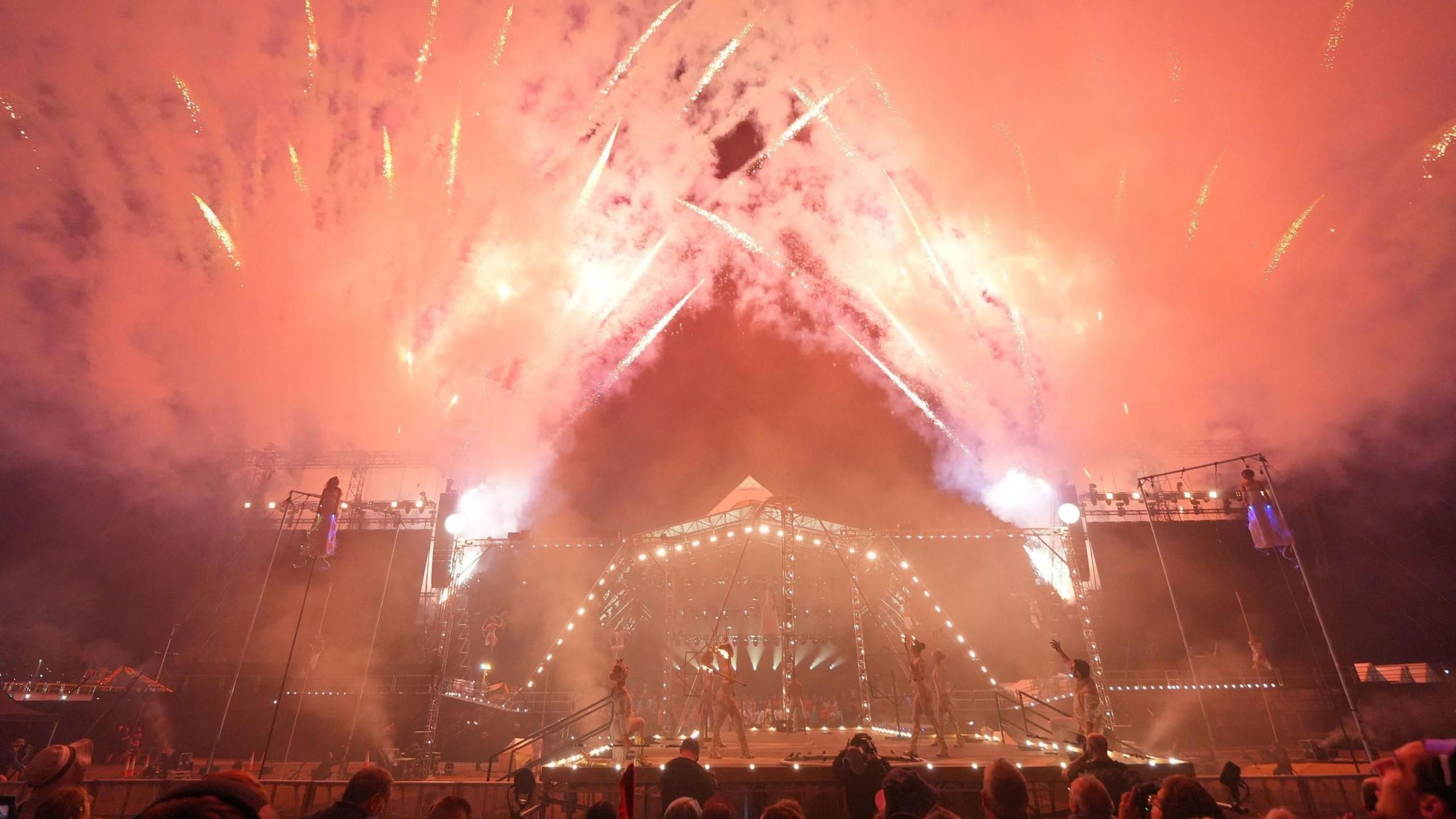 Acrobats and circus performers take part in the opening ceremony in the Pyramid Arena at Glastonbury Festival. There are red fireworks going off around the stage.