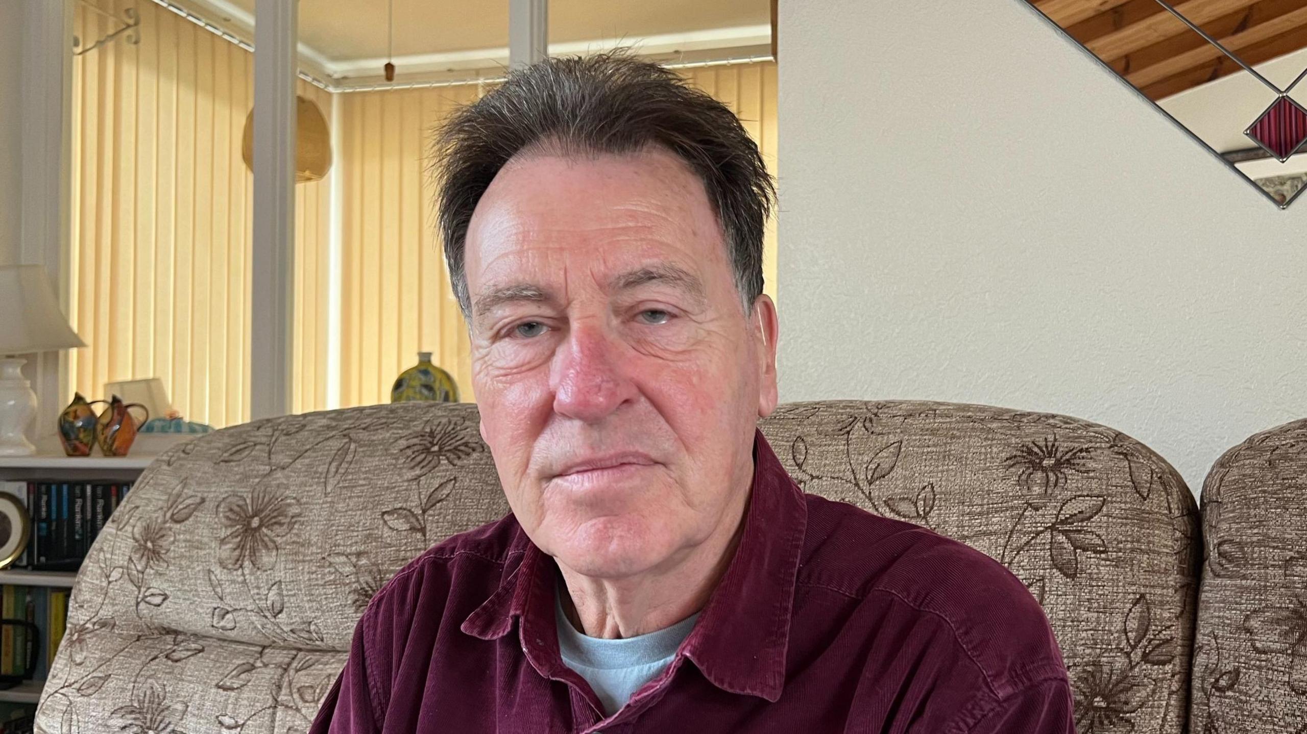 Steve Marsling sitting on a brown sofa wearing a maroon shirt.