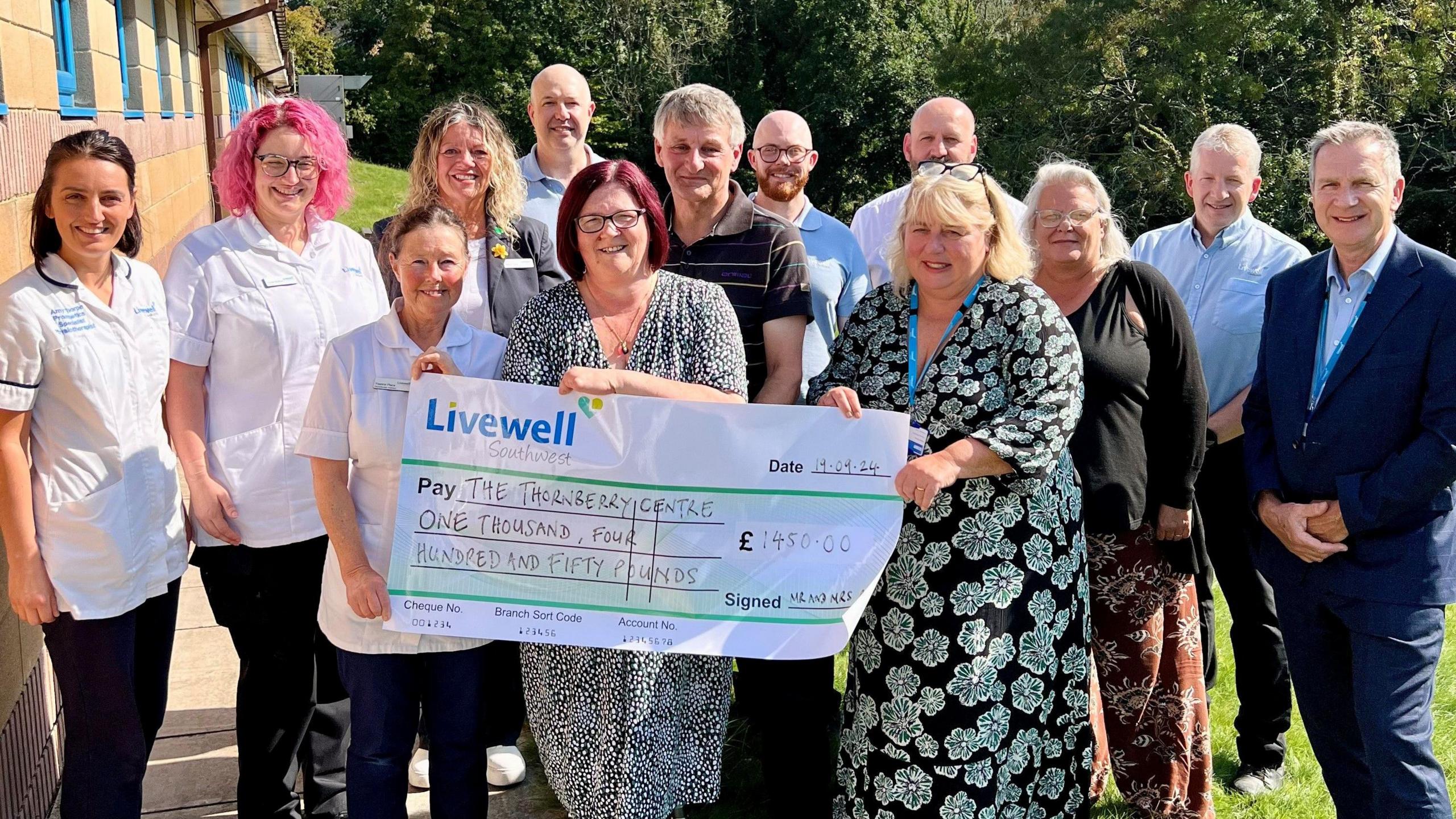 Large cheque being held up in front of a group of smiling people. 