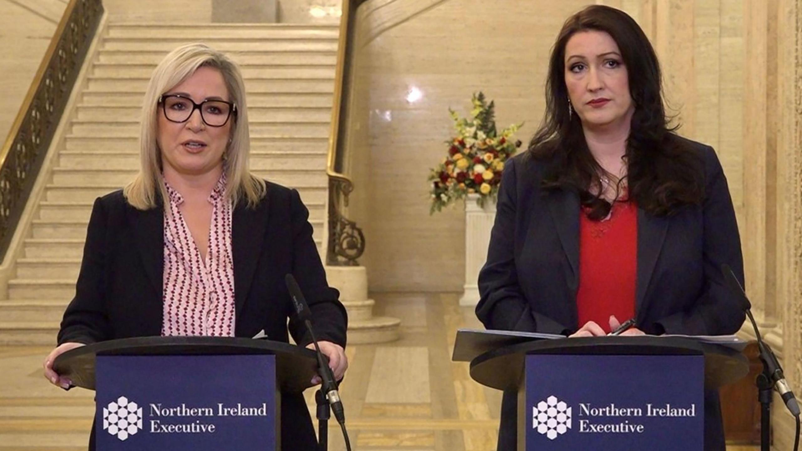 Michelle O'Neill and Emma Little-Pengelly pictured giving a joint press conference to warn the public about Storm Éowyn last month.  They are both wearing dark suit jackets and coloured blouses and they are each standing behind lecterns in the Great Hall in Stormont.