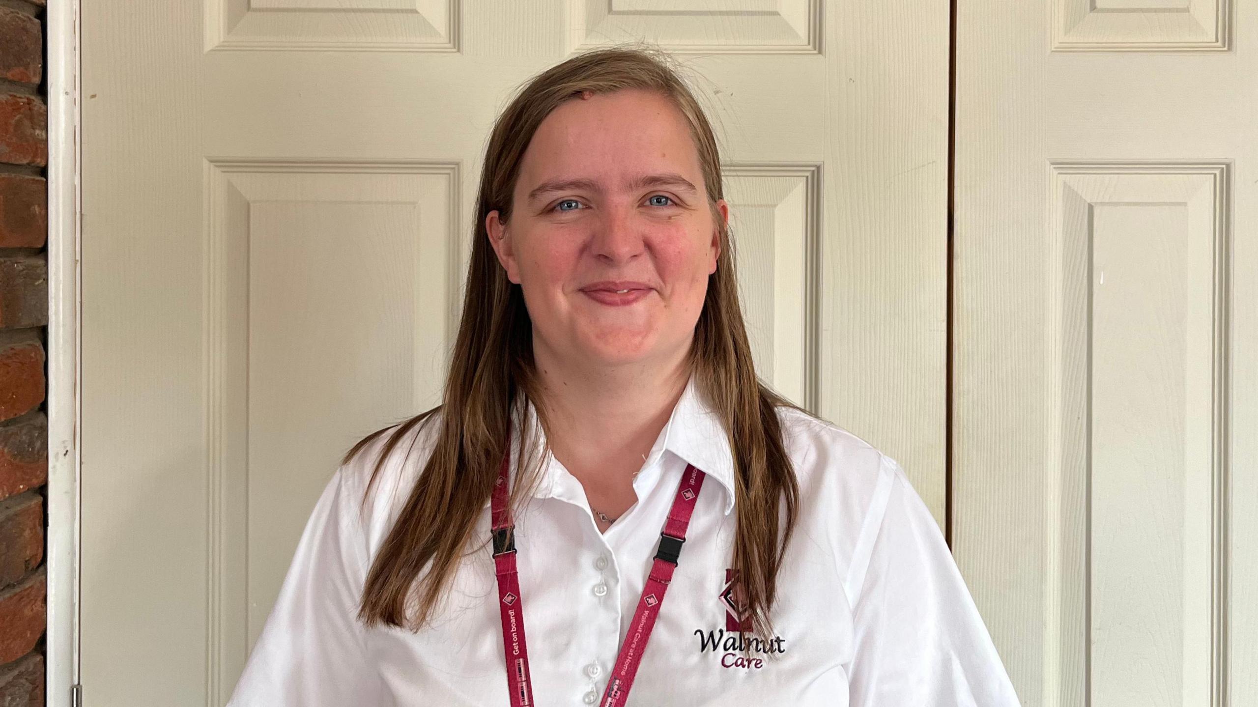 Alice Weatherley smiling at the camera. She has brown chest-length hair and is wearing a white shirt with a logo reading 'Walnut Care' on it. She is wearing a red lanyard around her neck.