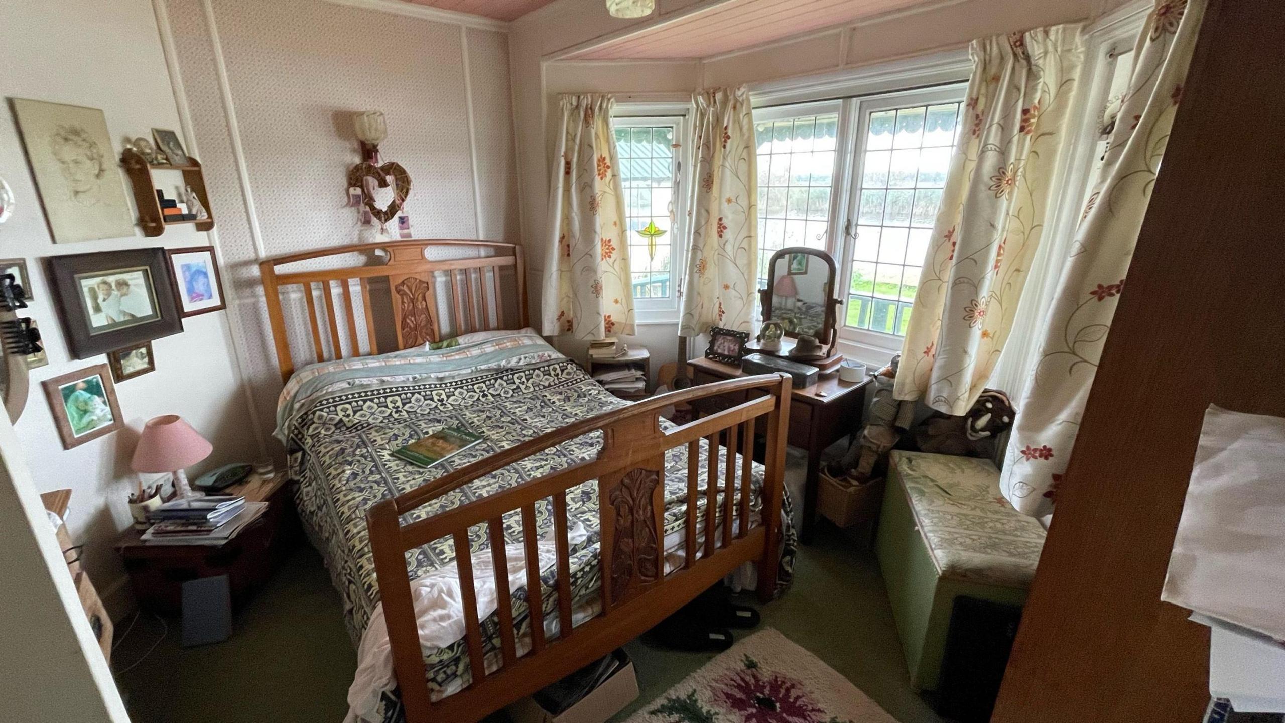 A bedroom at Towerview, showing a wooden bedstead. There are photographs on the wall and a bay window on the right overlooking the Broads