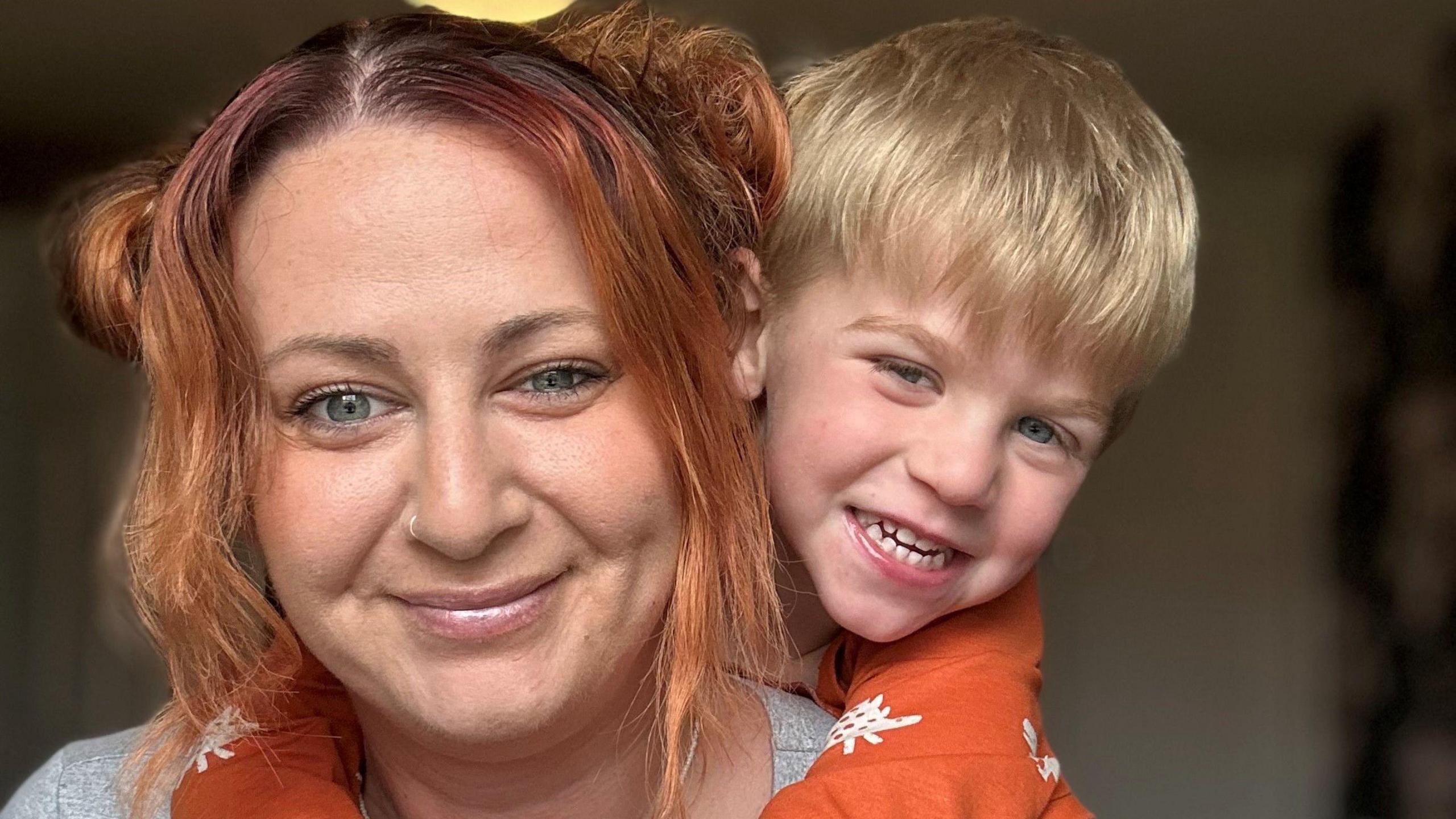 Sophie on the left smiling at the camera with ginger hair and one of her sons on her back smiling at the camera on the right