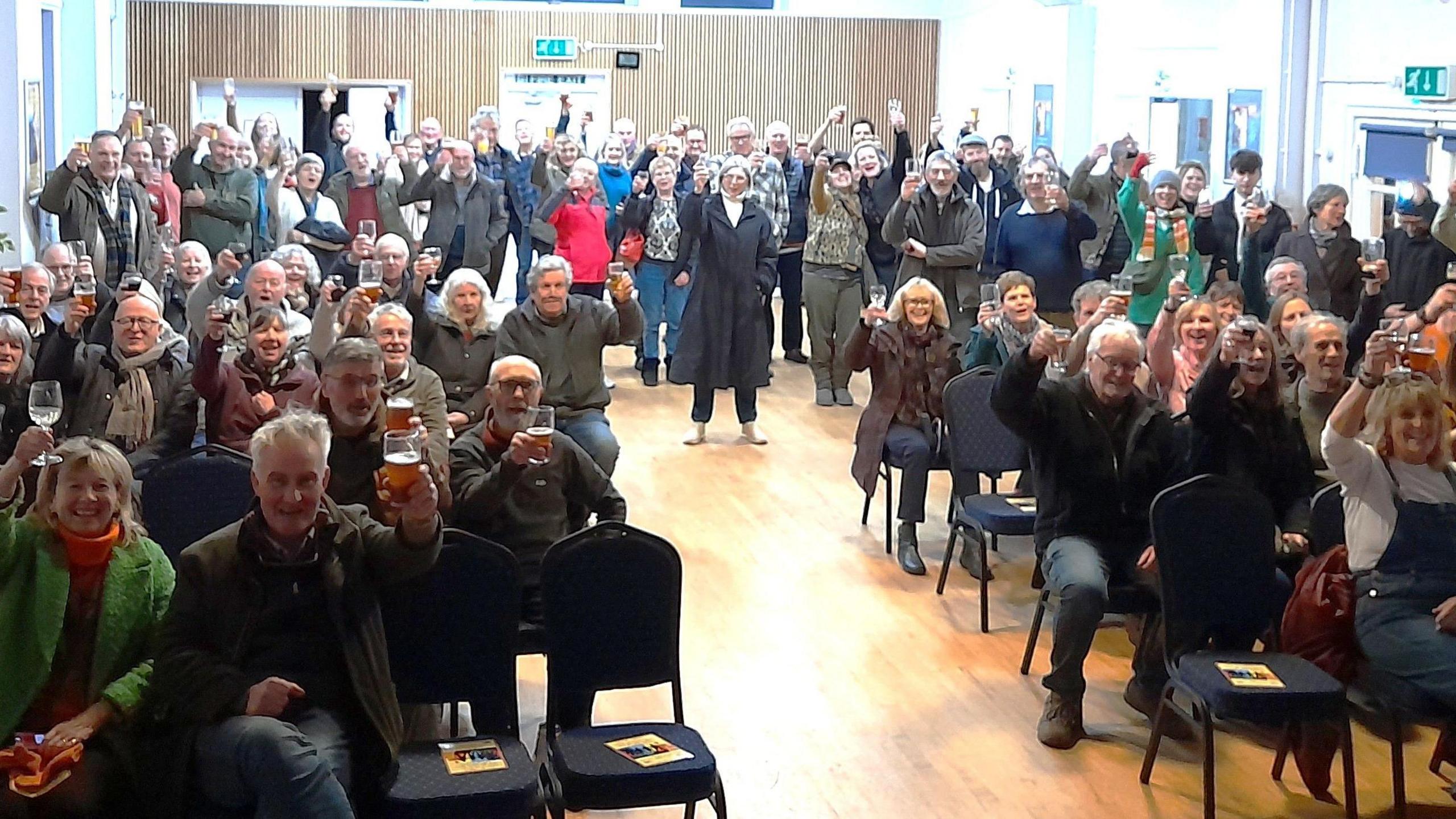 Group of people cheering to the camera in a community hall.