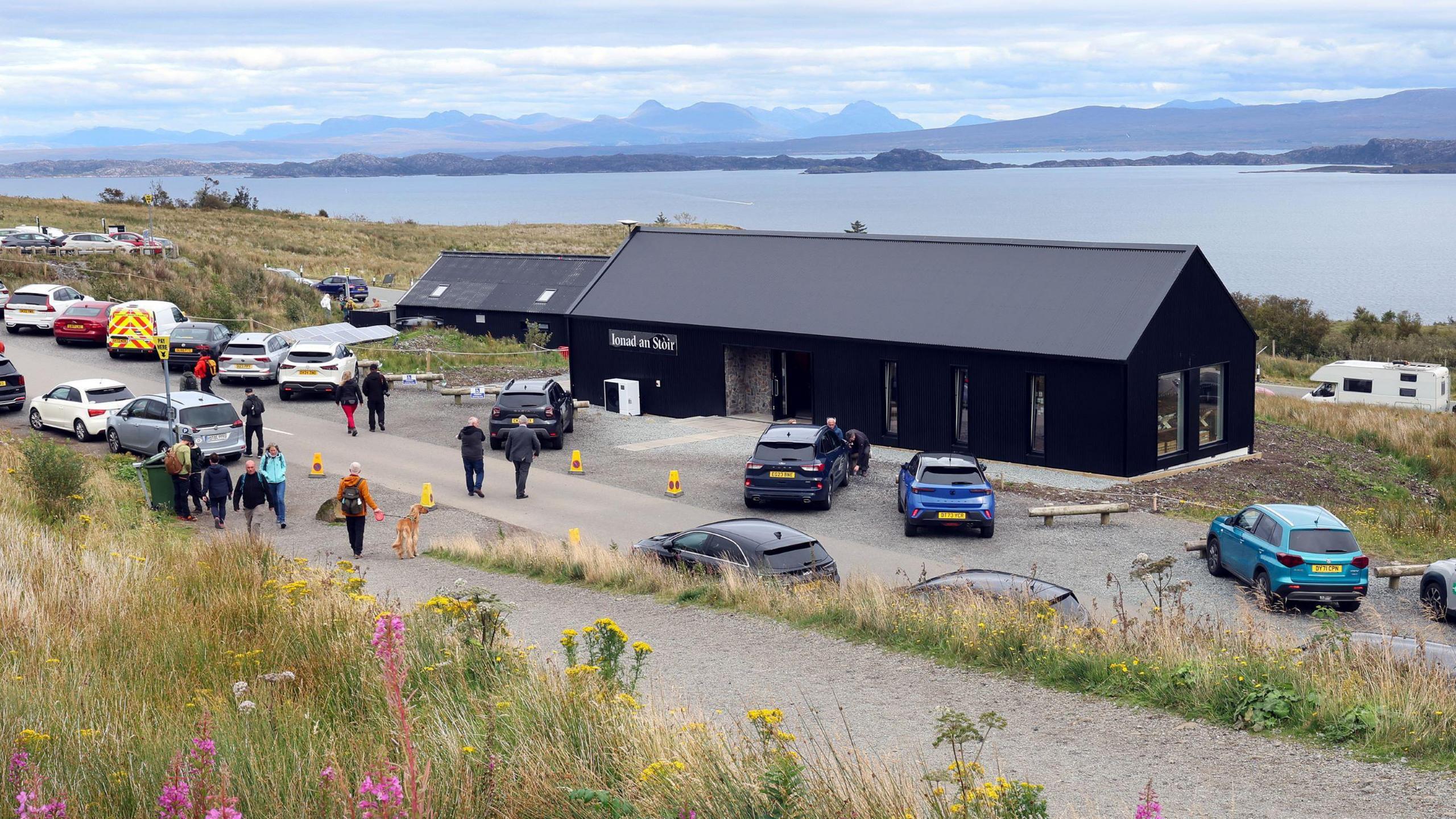 The recently built Storr centre can be seen. It is a long black building. Behind it lies the sea and the mountains of Wester Ross in the distance.