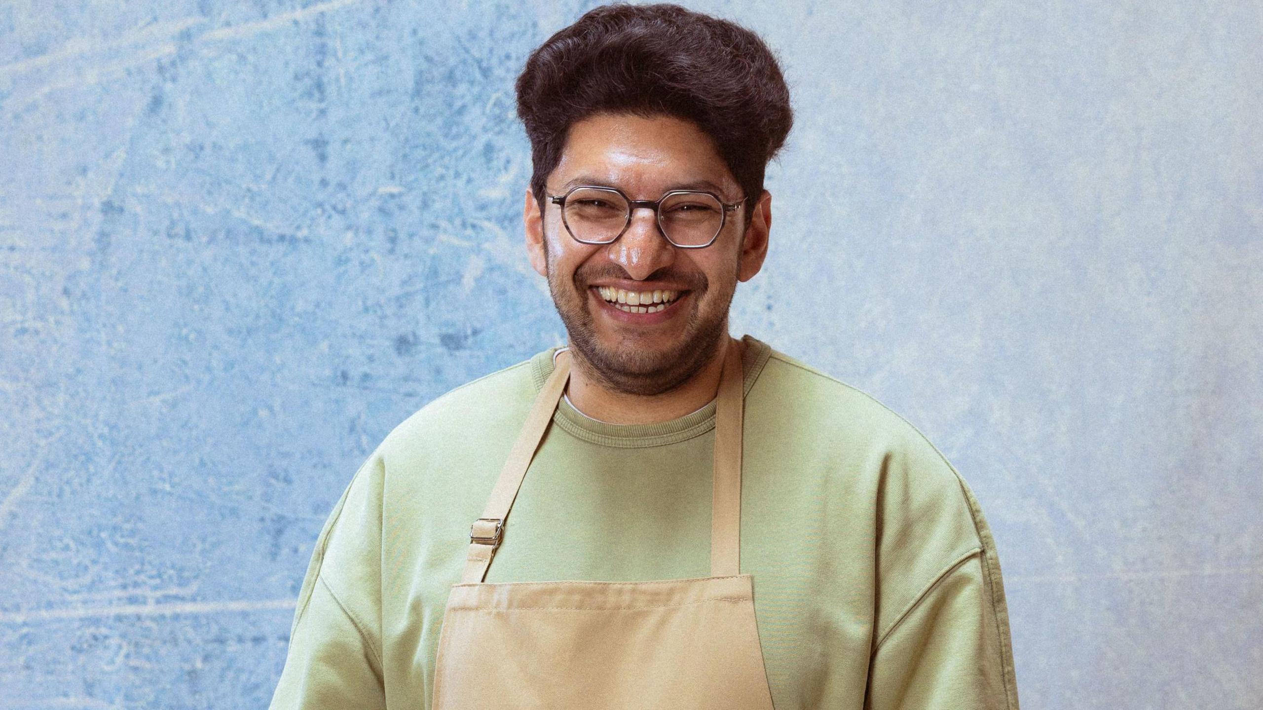 Hassan, a man of South Asian heritage, wearing an apron and laughing.