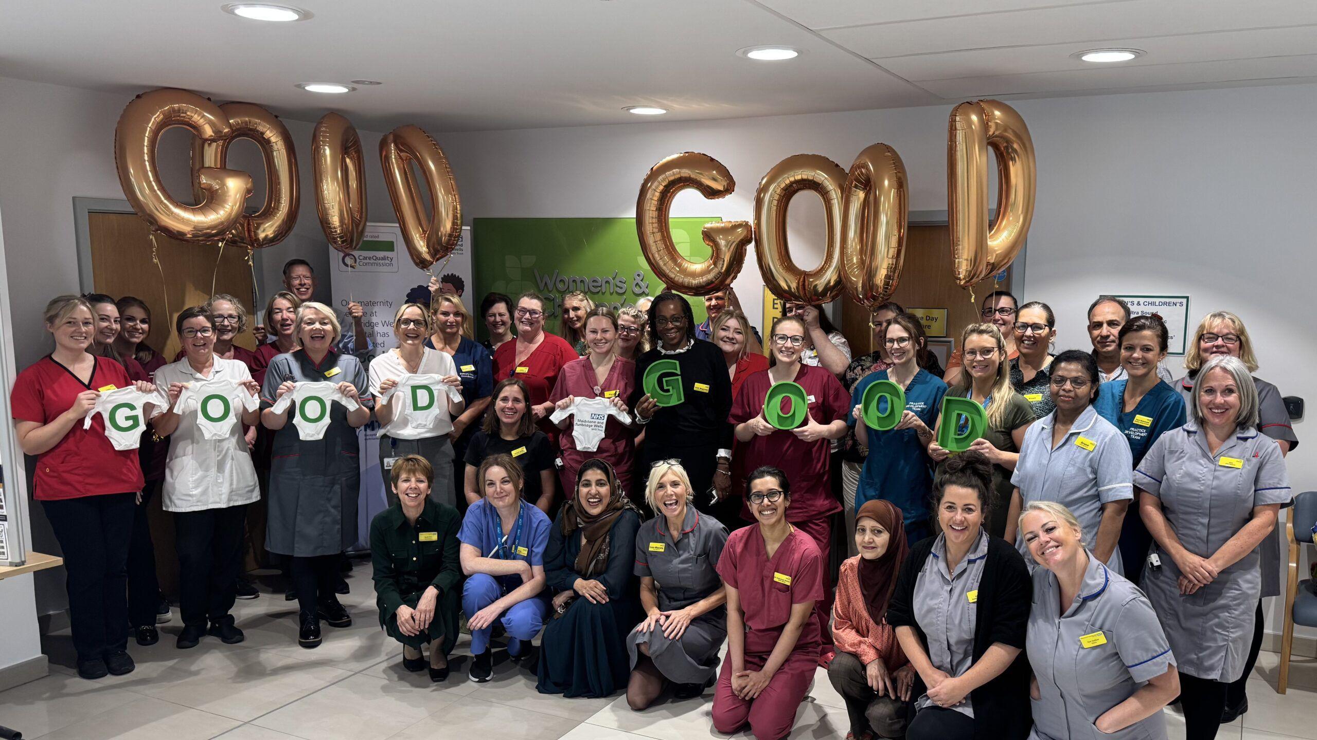 Dozens of staff at the Tunbridge Wells Hospital pose for a group photo, most wearing scrubs or tunics, some holding up golden balloons spelling out the word "good" twice over.