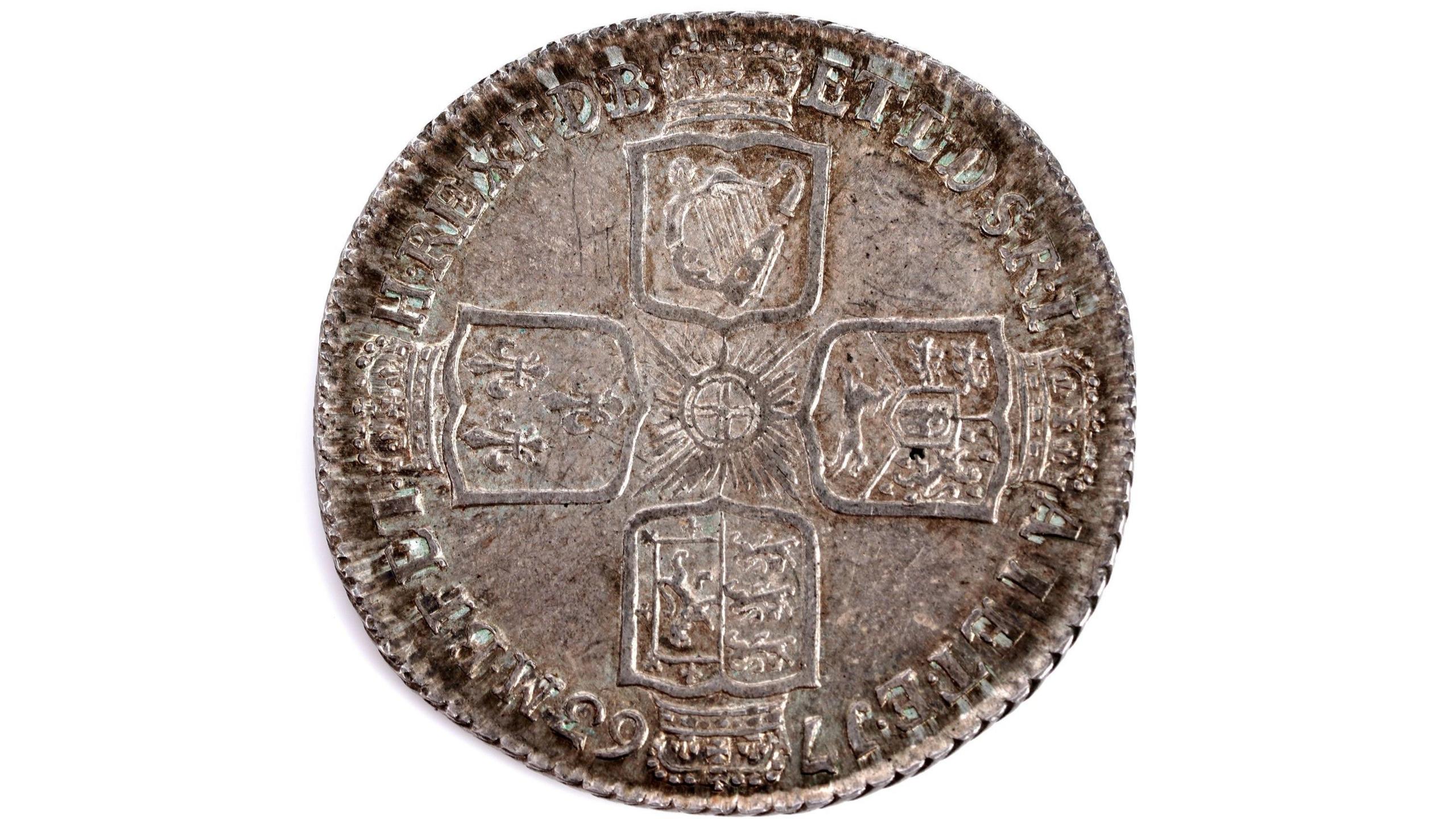 A round coin which is browning in colour and bears the image of four different crests.