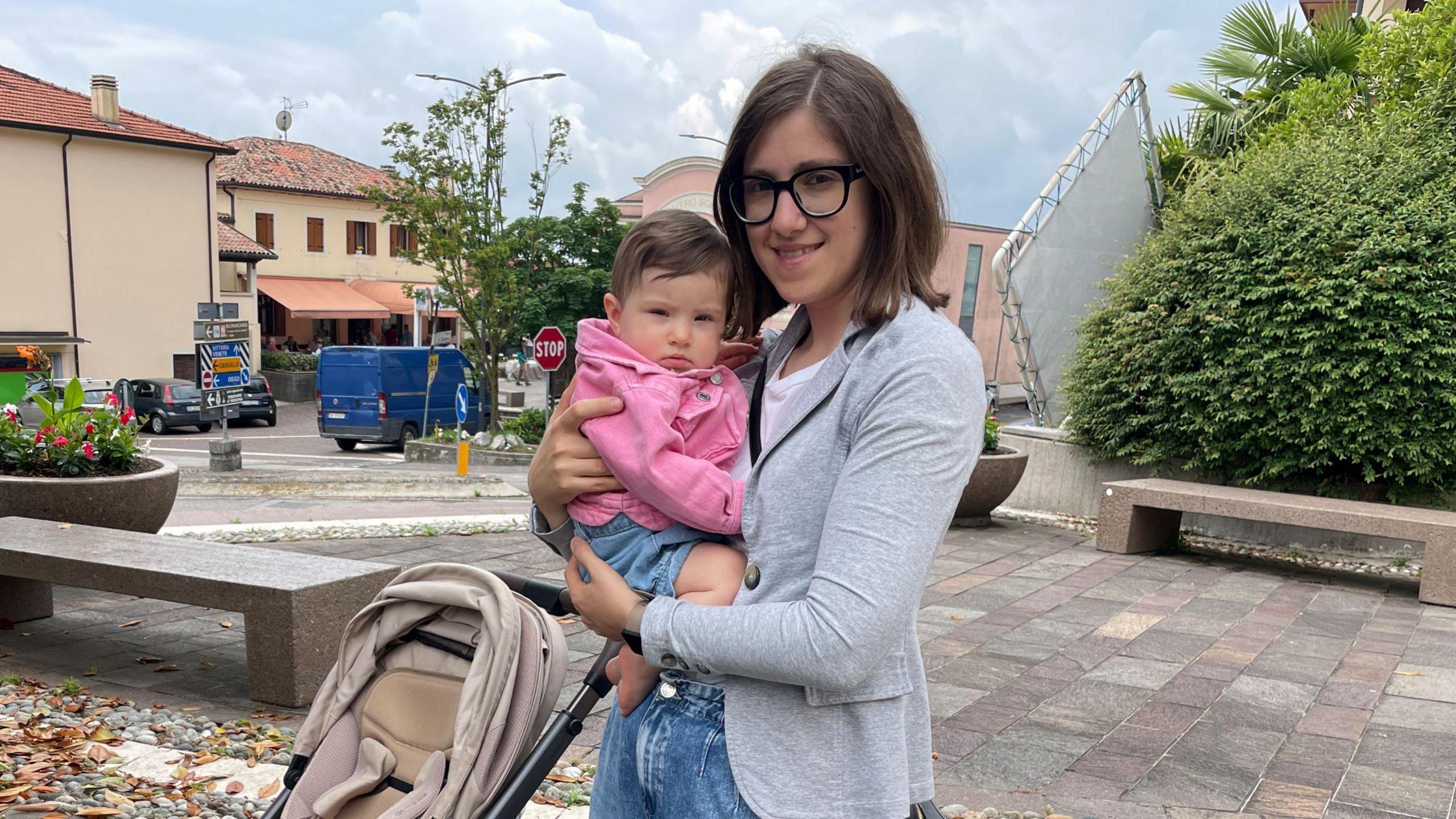 Valentina, a woman with dark hair and glasses, holds a baby in a pink jumper.