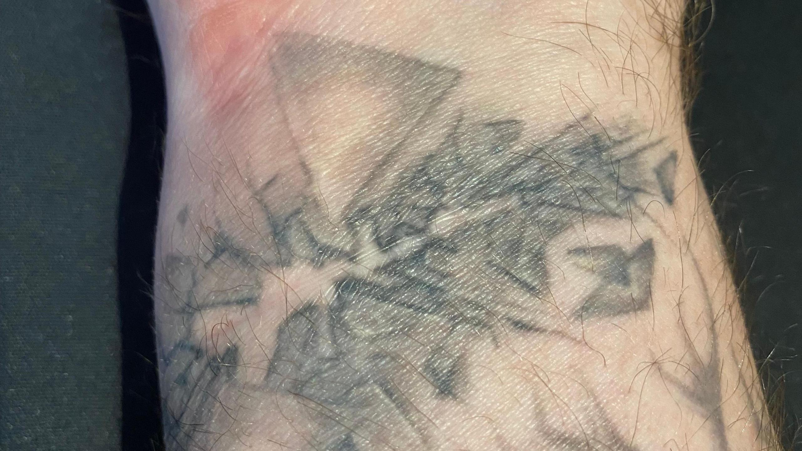 A close up image of a man's wrist with faded shards of glass tattooed around a faint horizontal scar