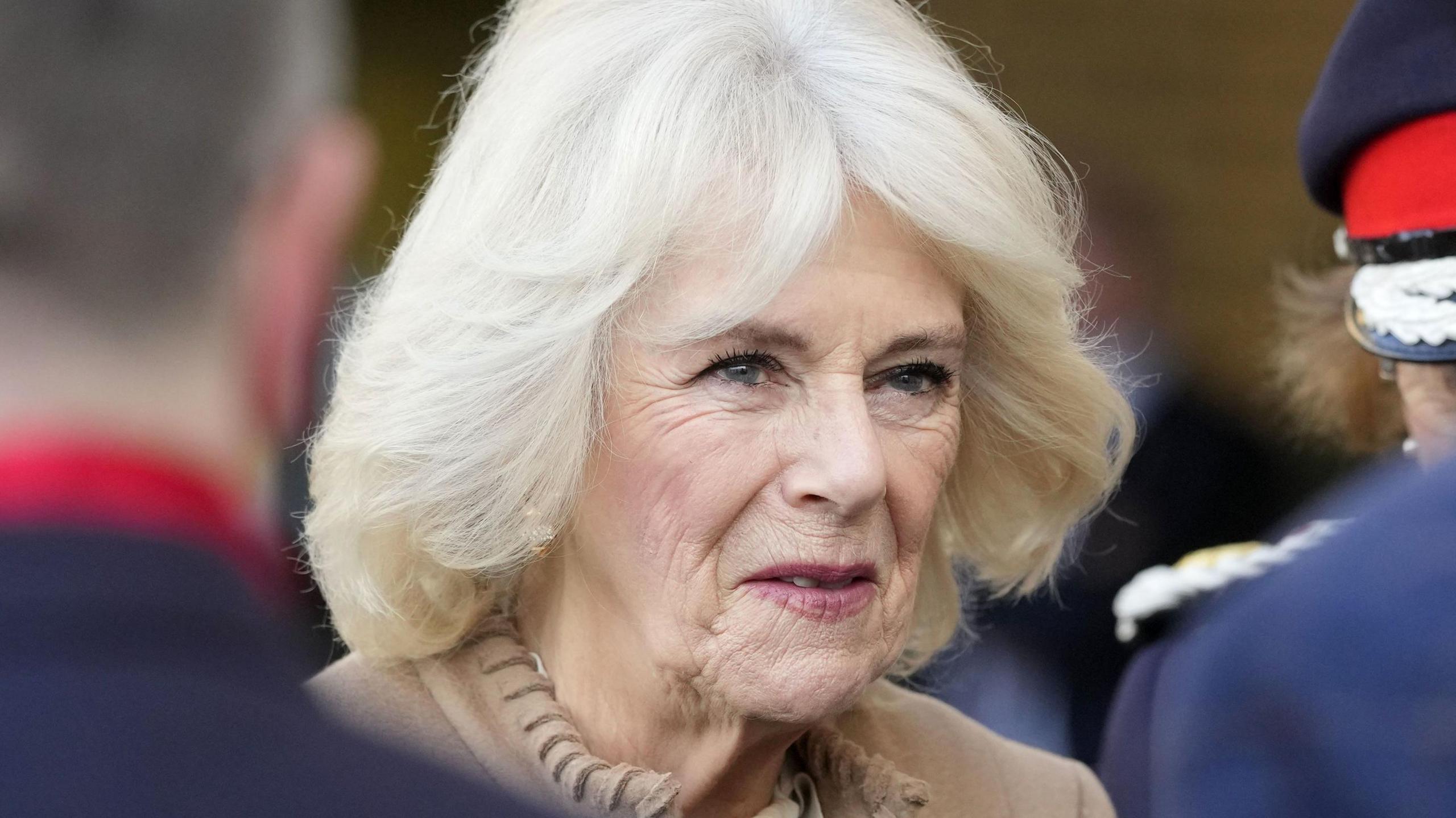 A photograph of Queen Camilla during a visit to the Swindon Domestic Abuse Support Service's (SDASS) in Wiltshire. She is wearing a beige-coloured top and is talking to two people in uniform who have their backs to the camera