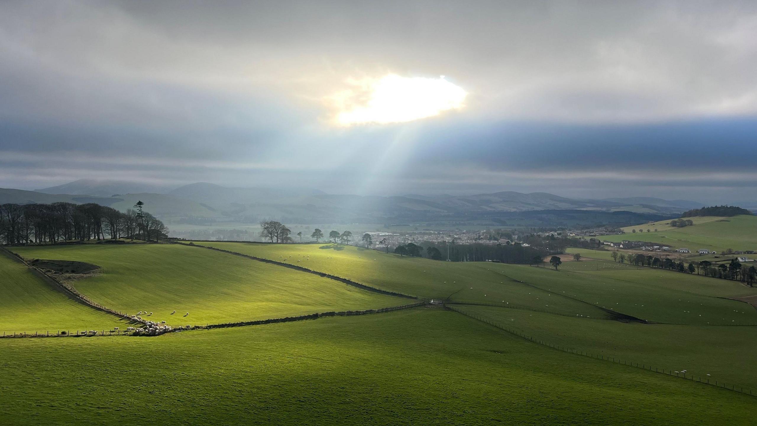 The sun shines through a gap in the clouds onto a green field