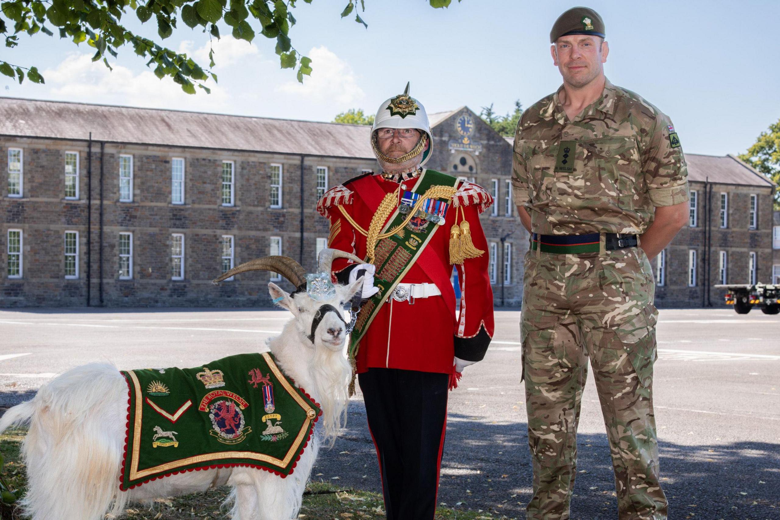 Jones in military uniform next to man in red ceremonial military uniform and a military goat.