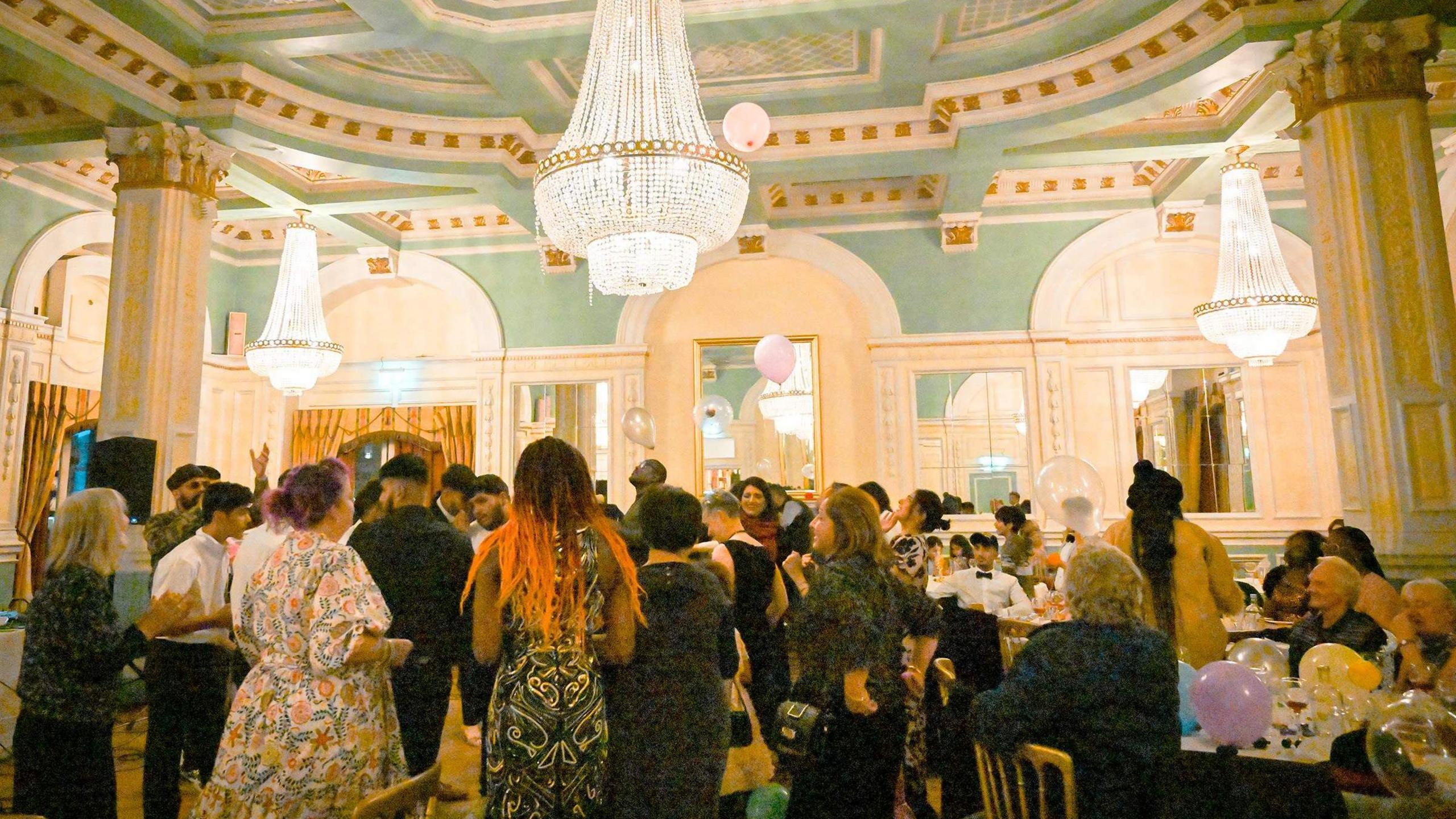 Scores of people dressed up standing in a hotel ballroom