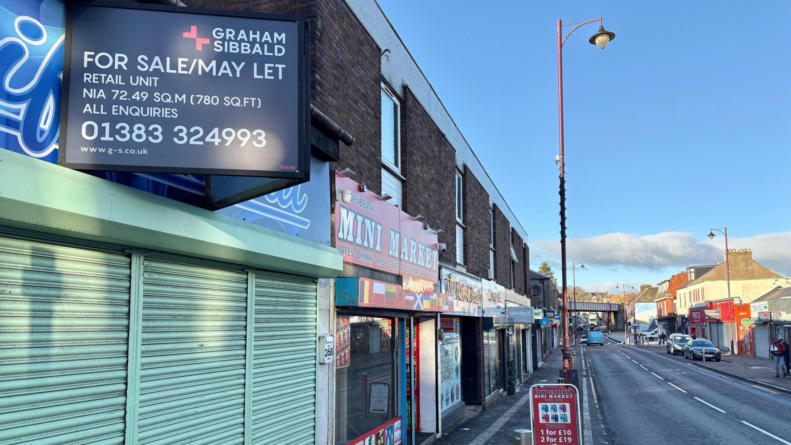 There is a green shuttered shop in the foreground. The street stretches into the distance.