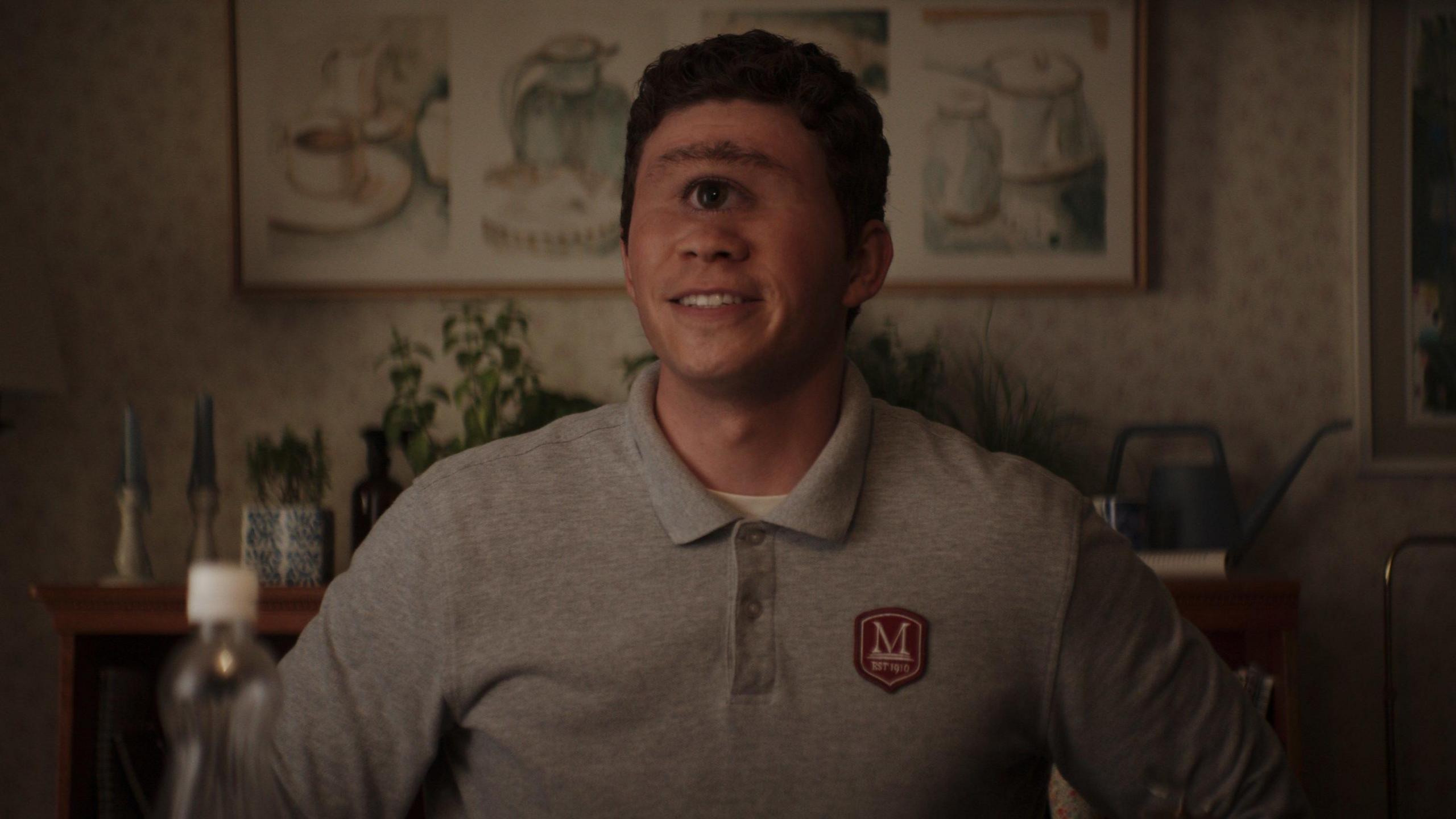 A young cyclops wears a grey polo jumper and smiles at the camera