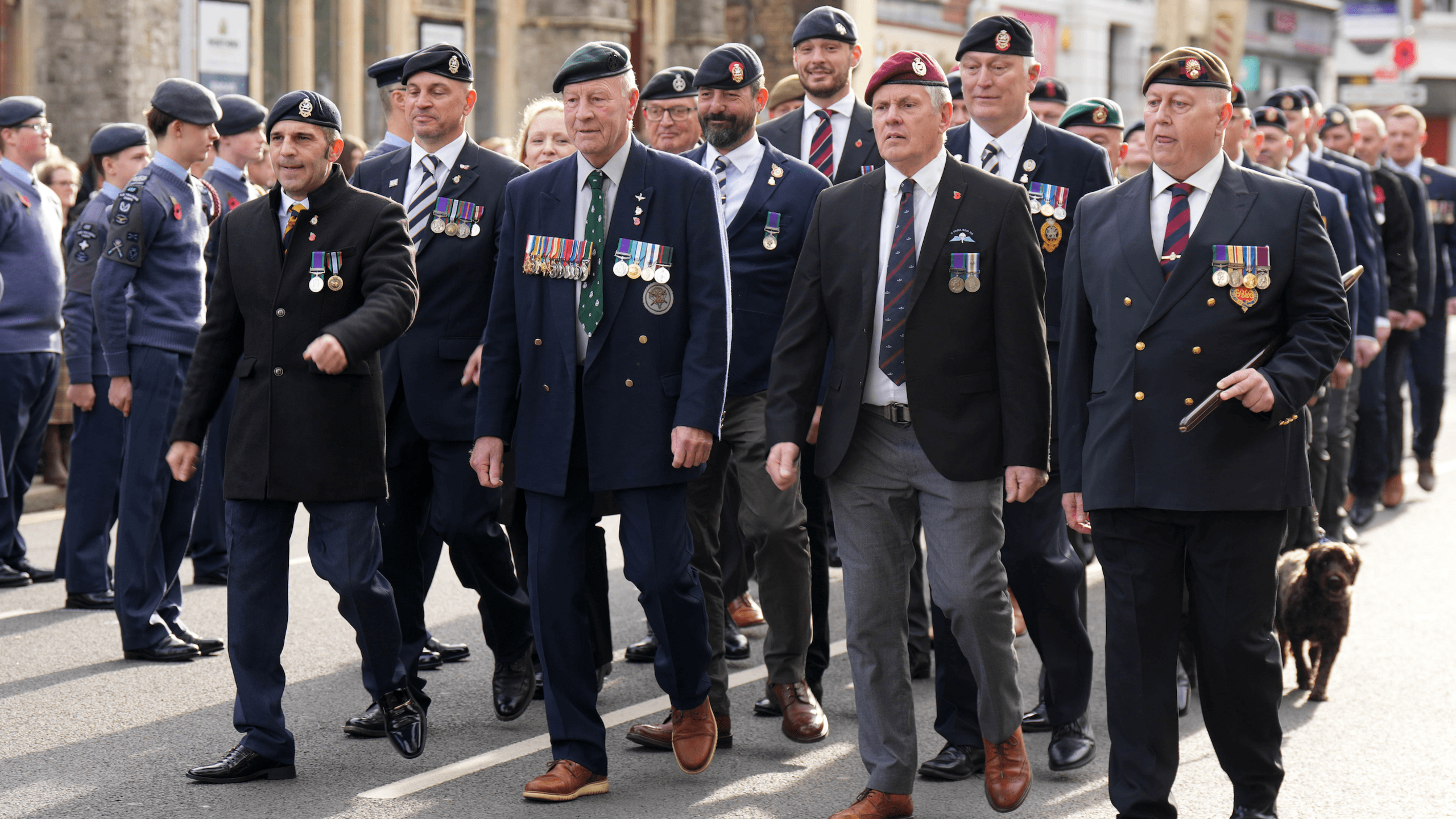 Veterans wearing medals and berets marching along a street