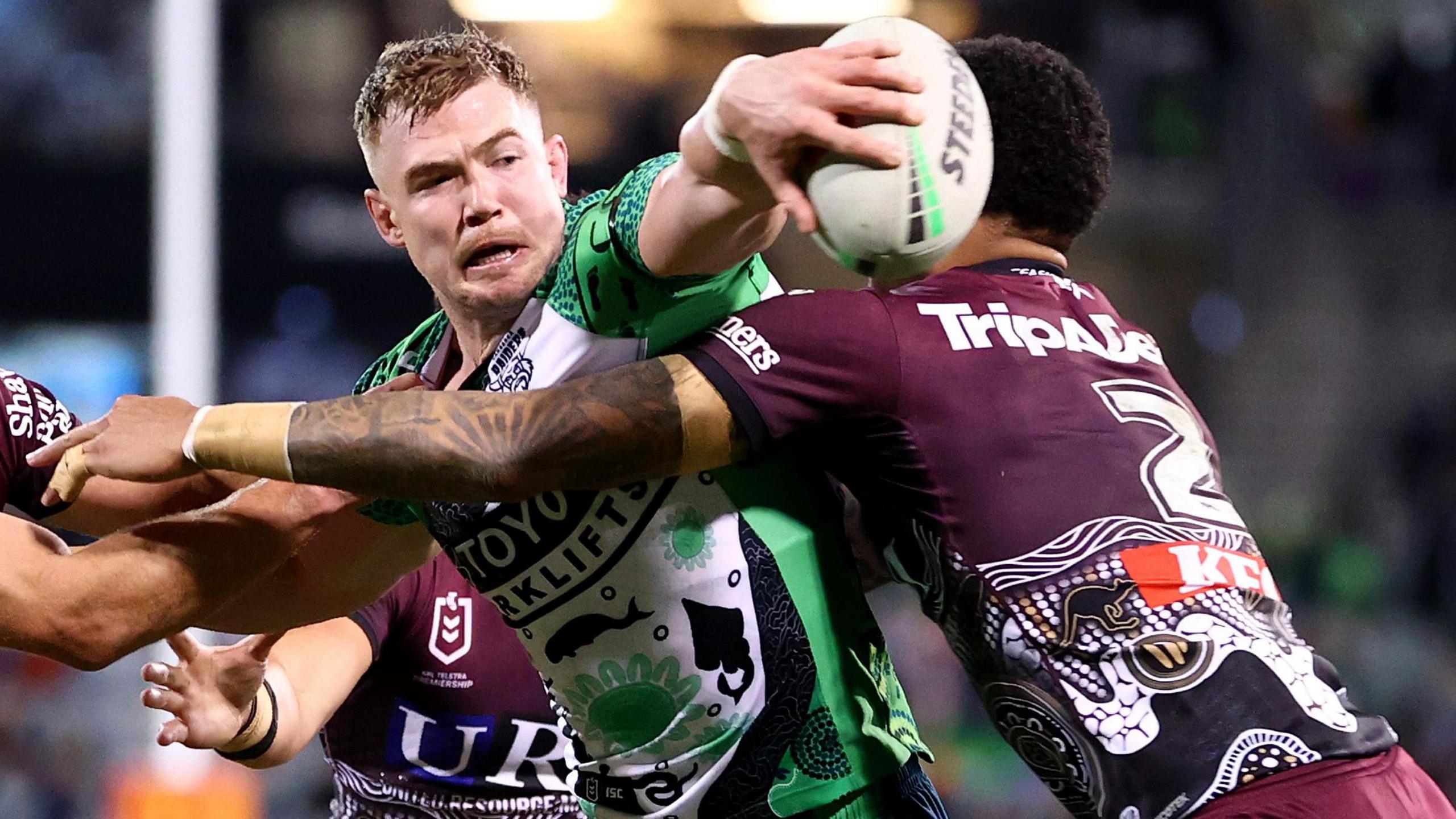 Hudson Young reaches out over the tackle of a Manly opponent to offload for Canberra in the NRL