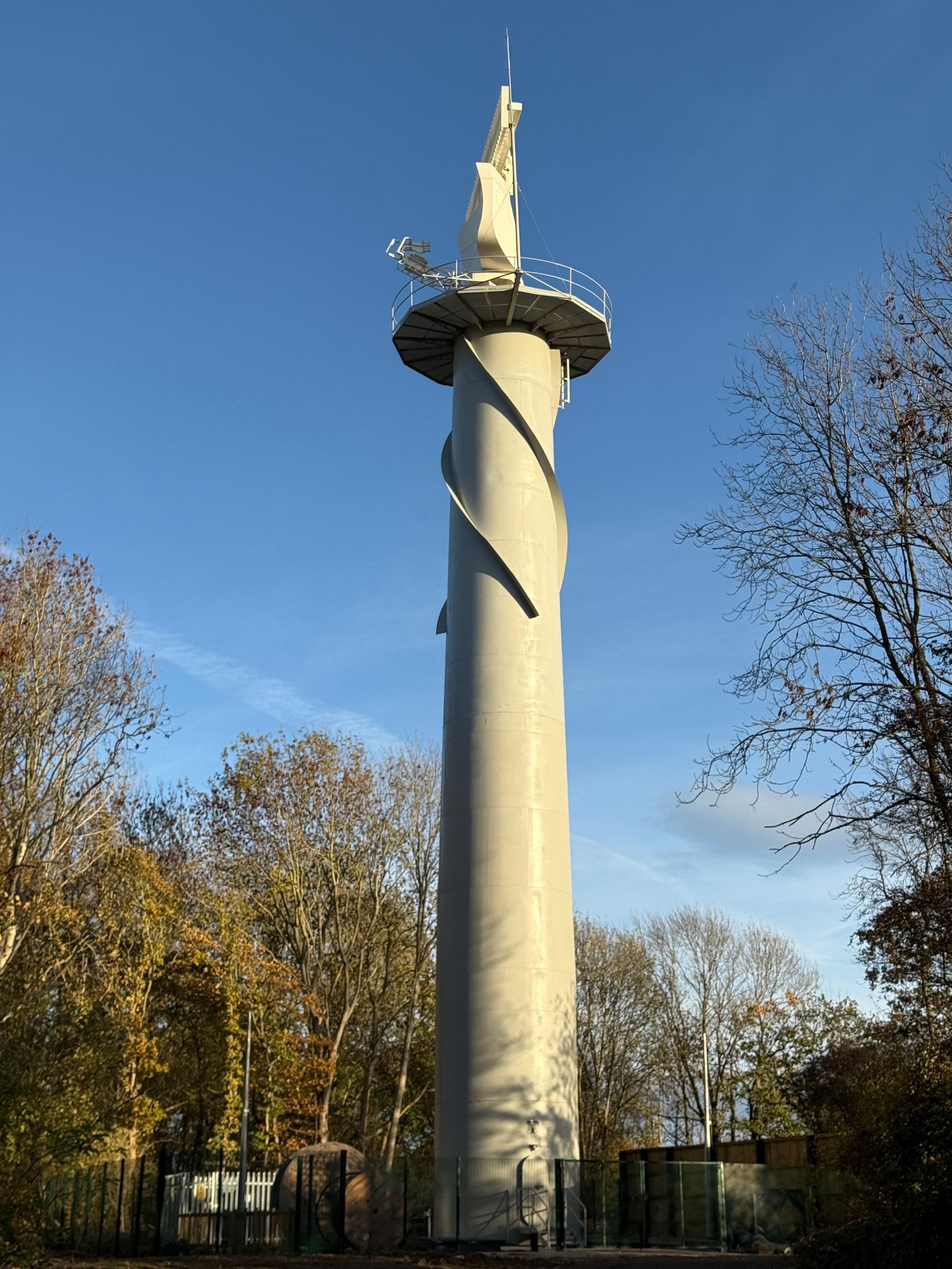 A radar control tower with trees surrounding it and blue sky above.