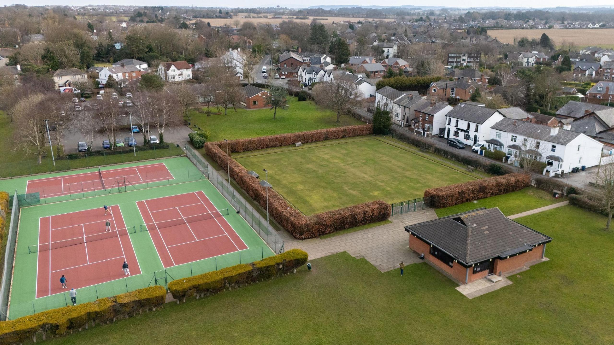 aerial drone image of Aughton village with people playing on tennis court, next to fields and white houses