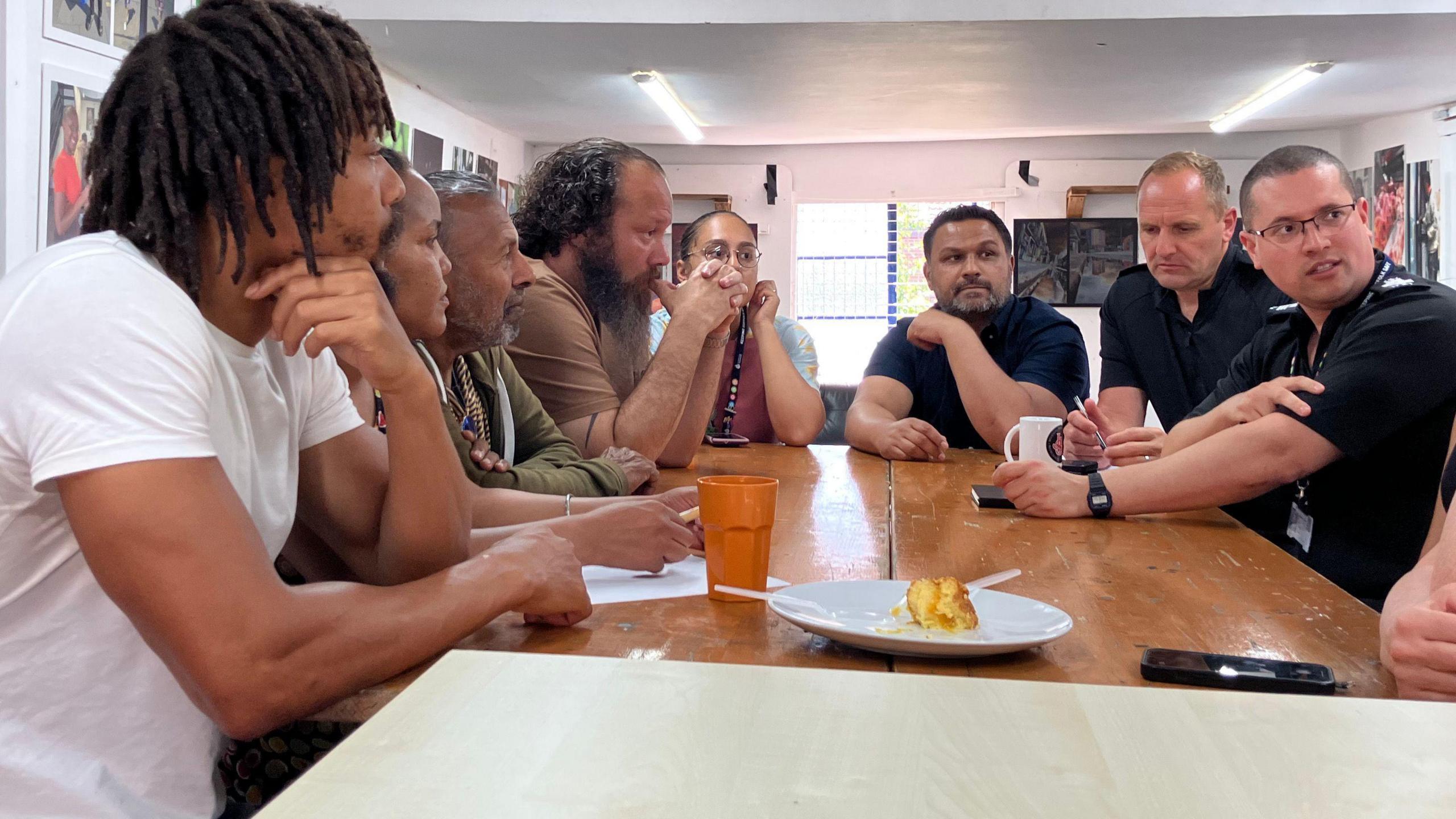 Eight people sit round a table, some are in police uniform