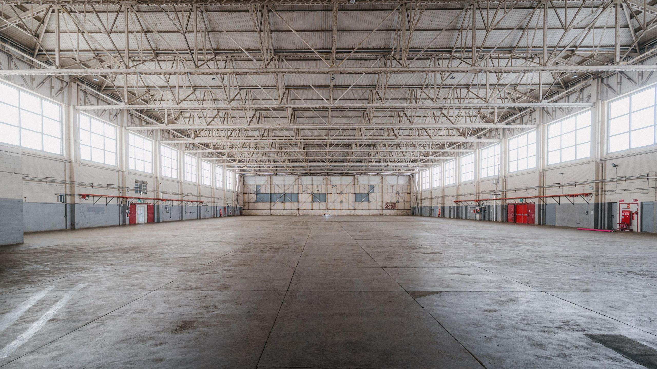 Inside a large former RAF hangar - it is empty.  The floor is smooth and the ceiling has line sof metal struts along its length.