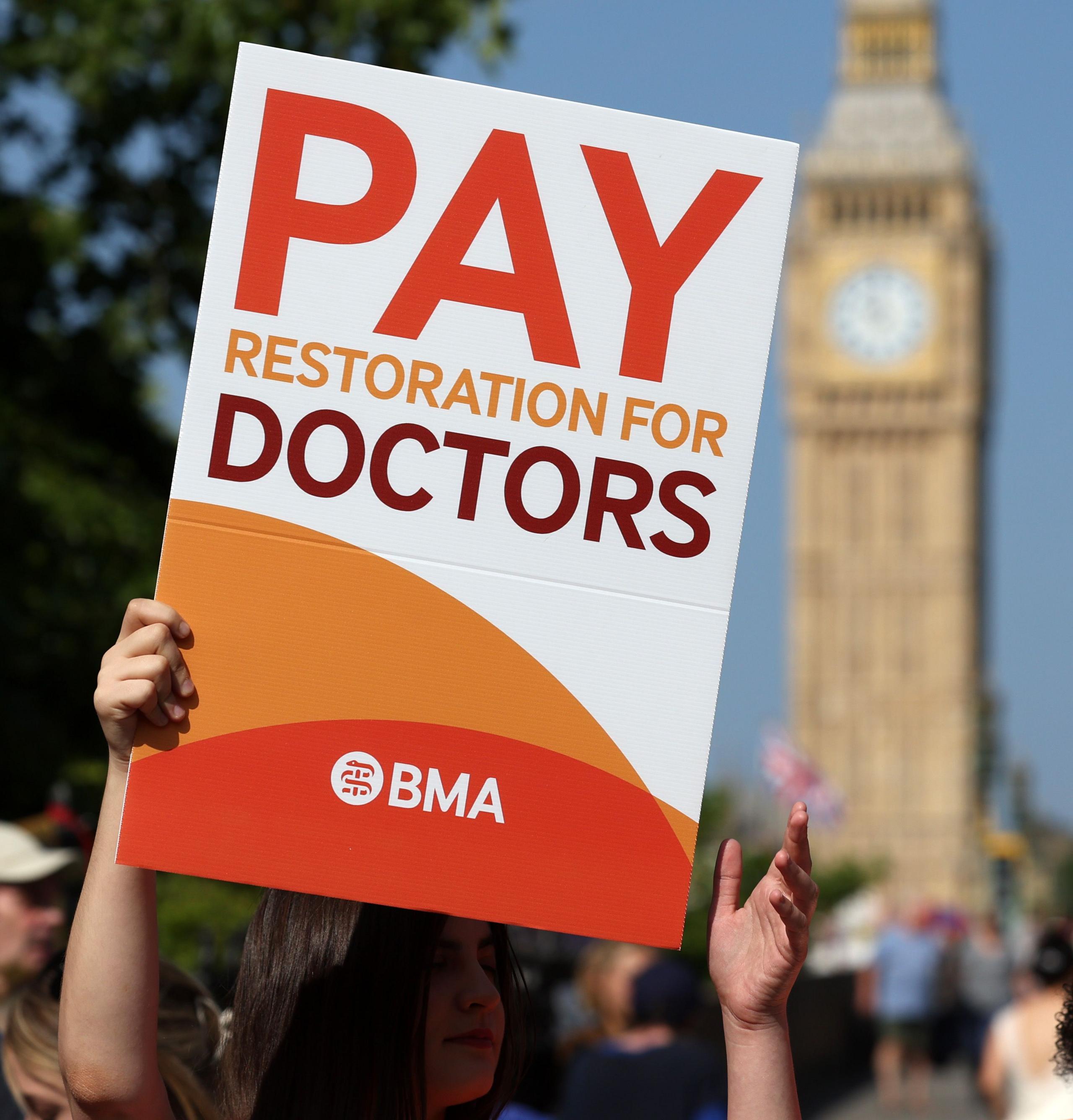 a close up of a placard that reads pay restoration for doctors with the houses of parliament in the background.