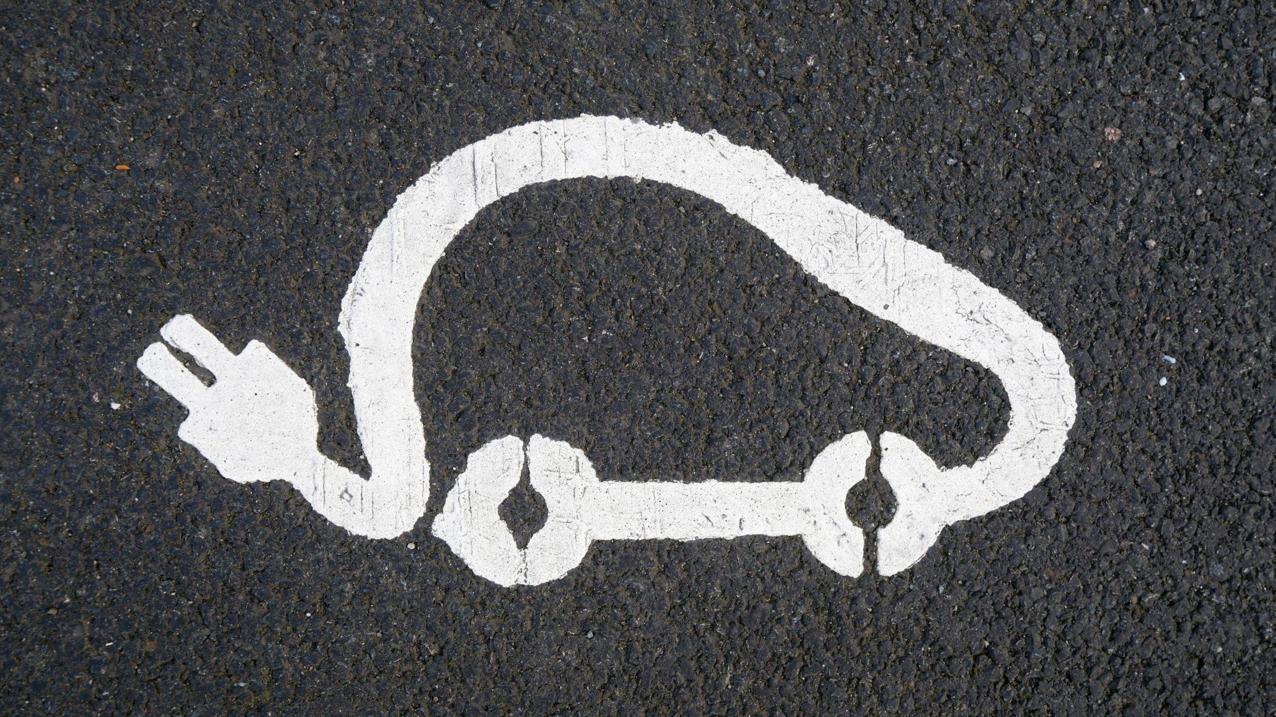The outline of an electric vehicle is marked in white paint on a grey section of tarmac.