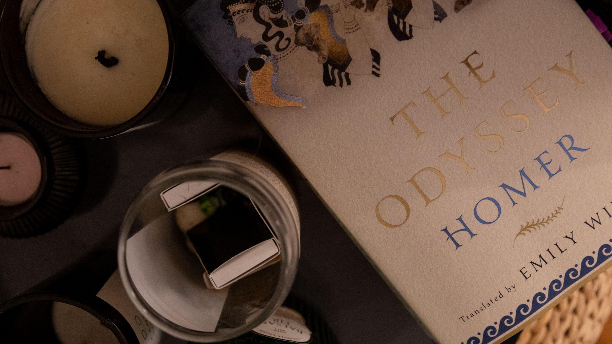 A photo of a copy of Emily Wilson's translation of The Odyssey on a table along with a candle and other items